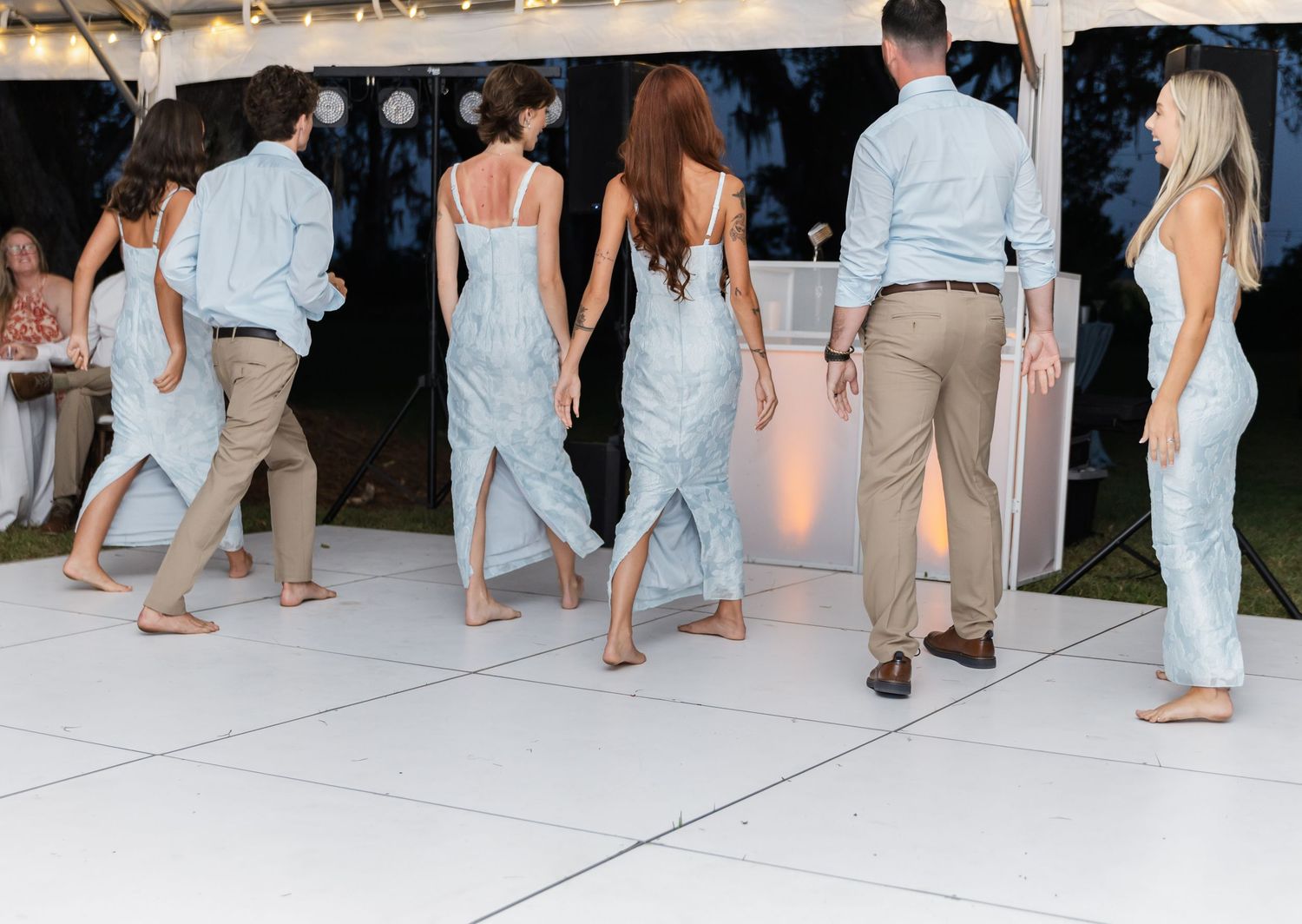 Wedding reception guests dancing on a white dance floor under string lights at dusk.