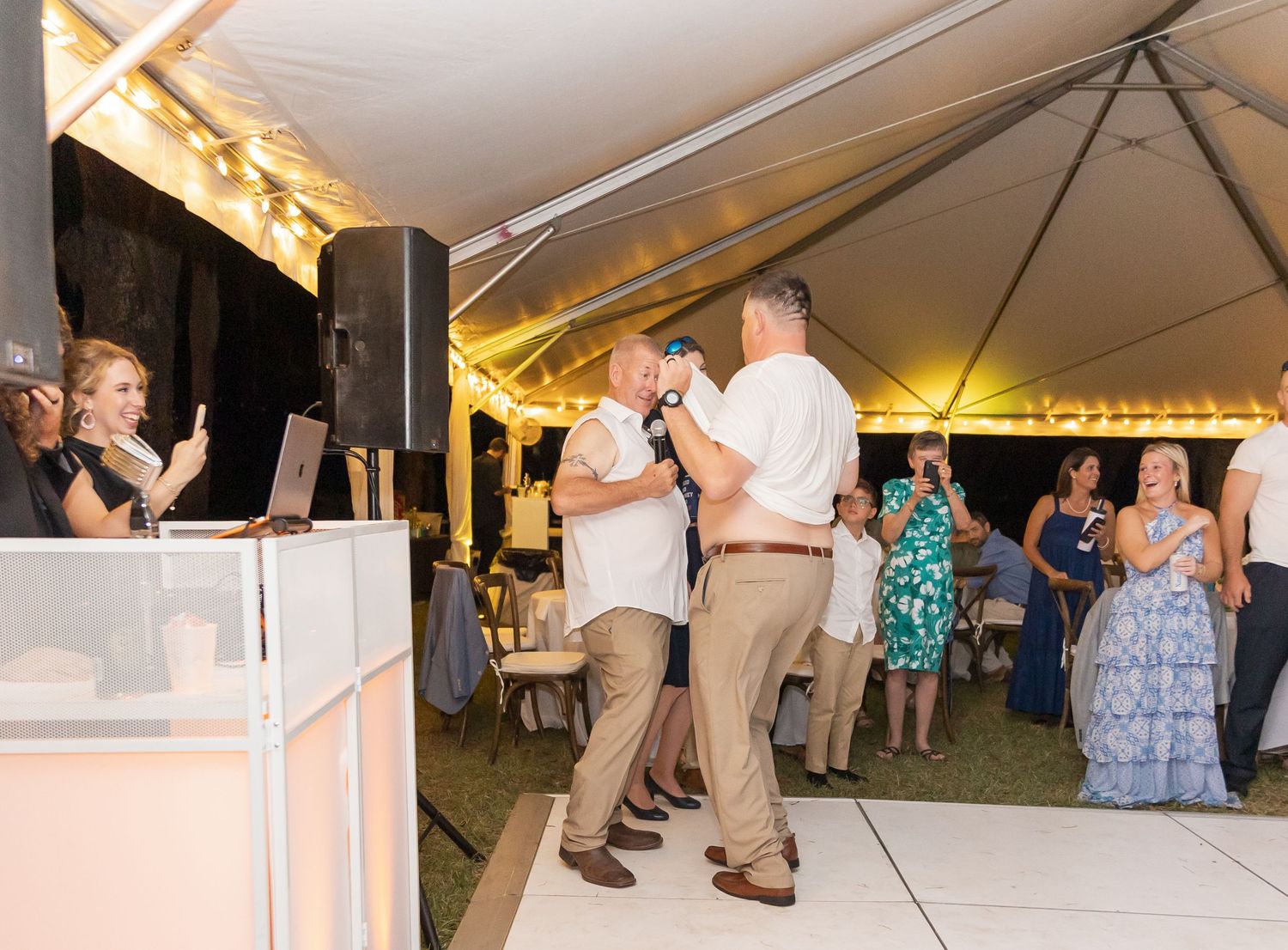 People dancing on a white dance floor under a large outdoor tent at an evening event.