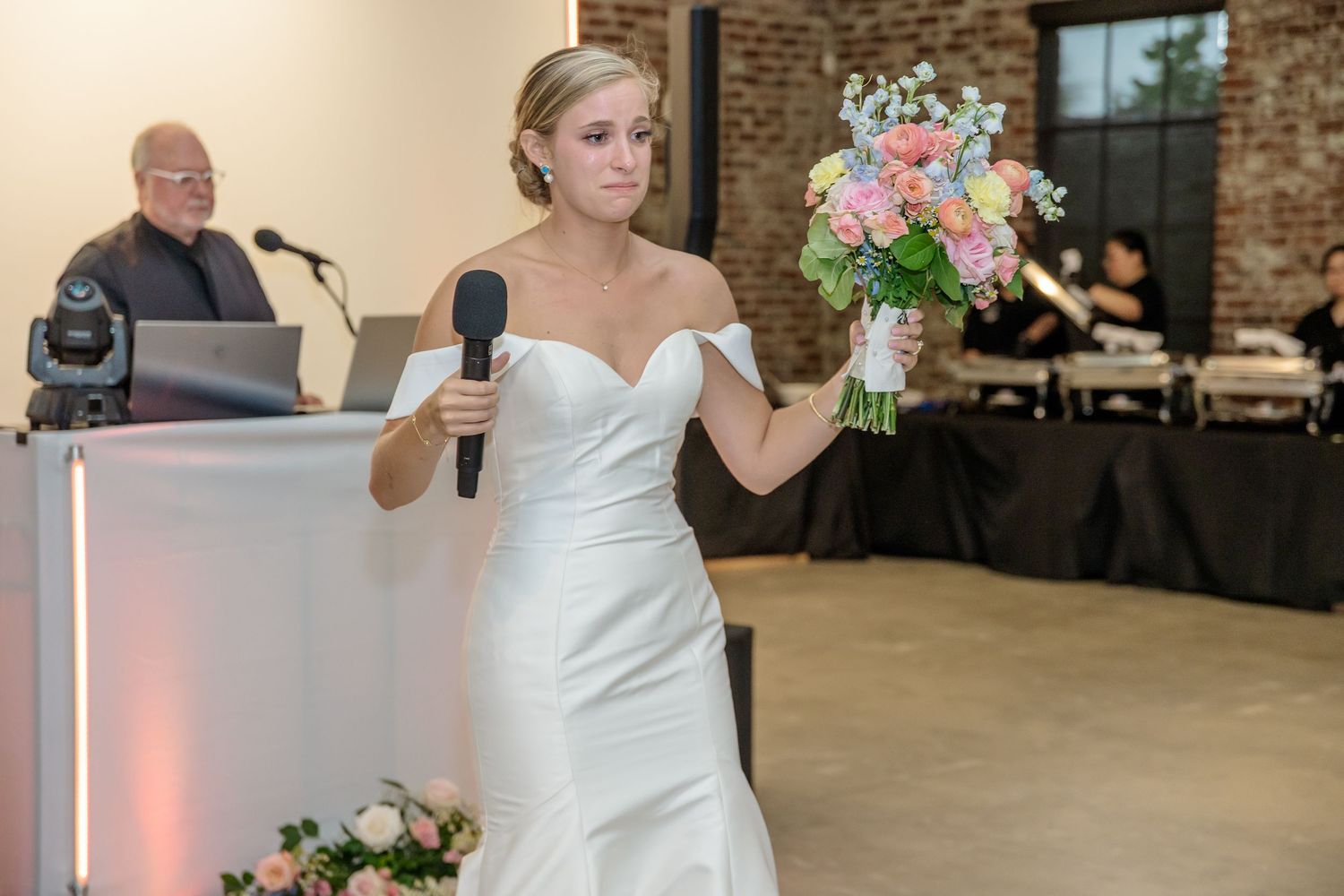 Wedding celebration in industrial venue with DJ setup and floral arrangements.