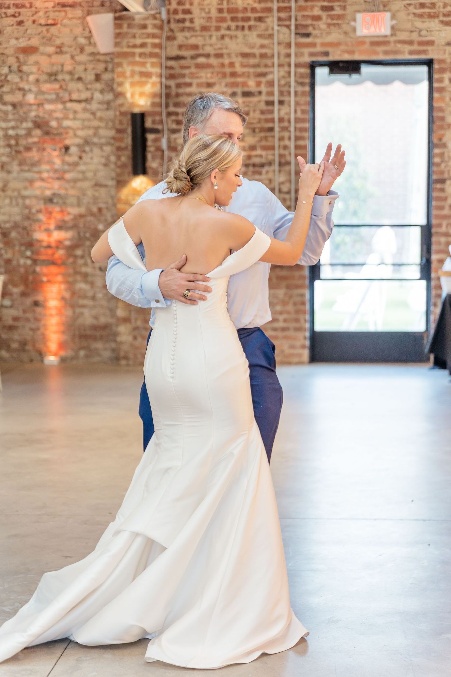 A bride in a flowing white wedding dress twirls gracefully on a dance floor inside a rustic brick-walled venue.