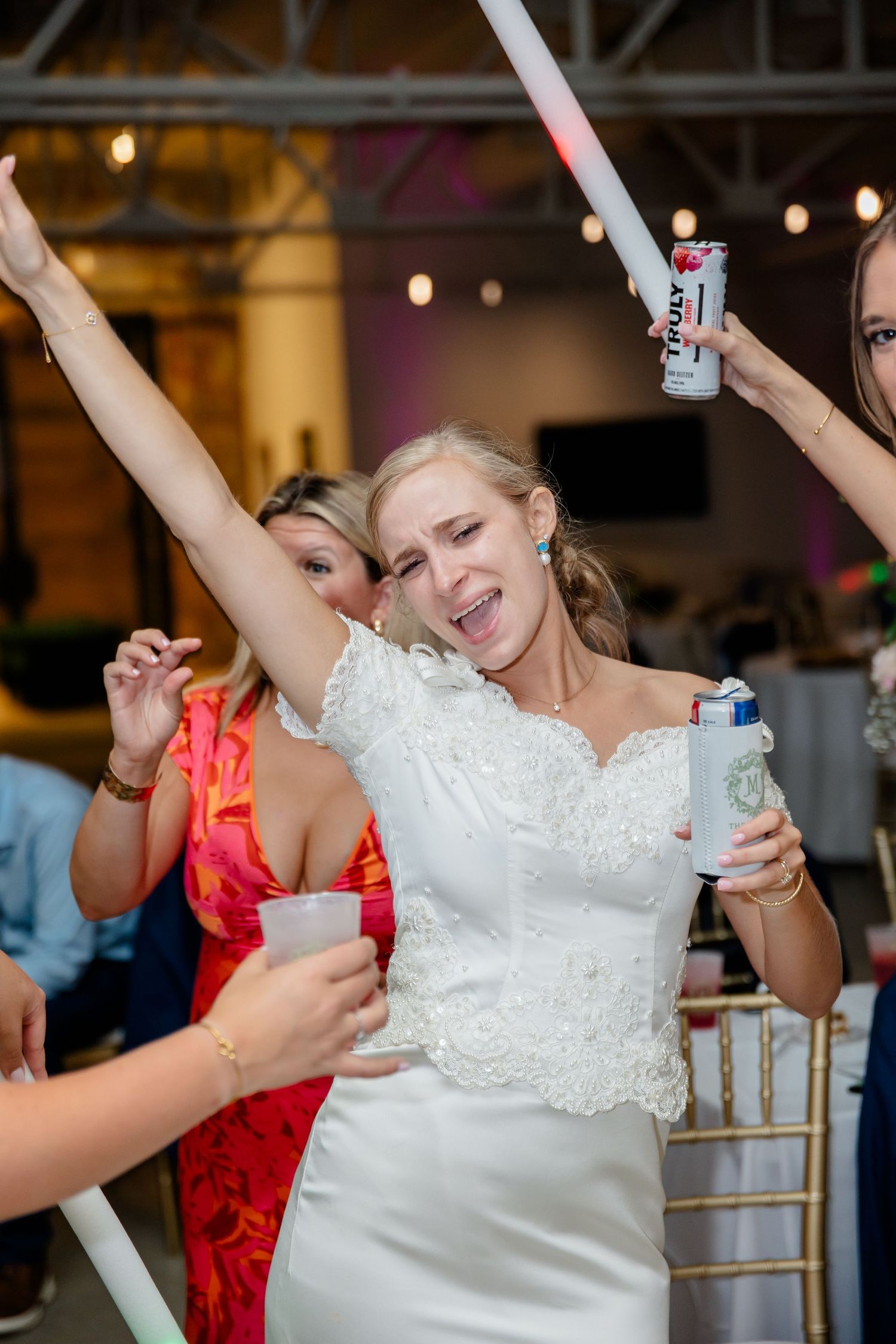 Bride and wedding guests dancing with glow sticks under ambient lighting at reception.