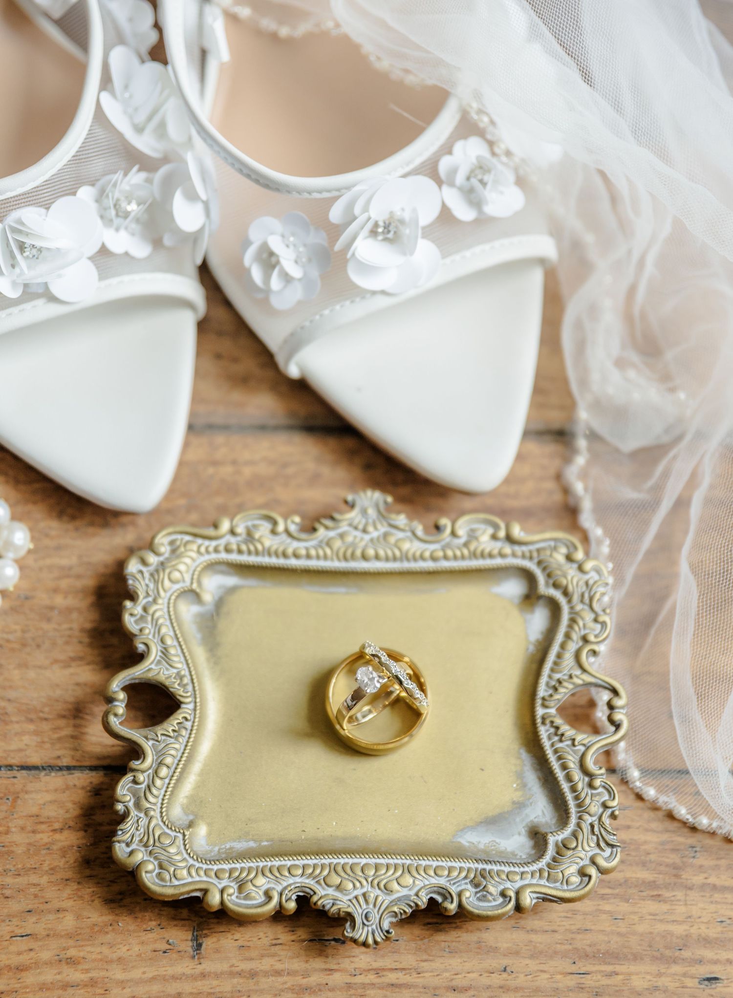 Wedding rings displayed on an ornate vintage silver tray with delicate floral details and a cream-colored velvet interior.