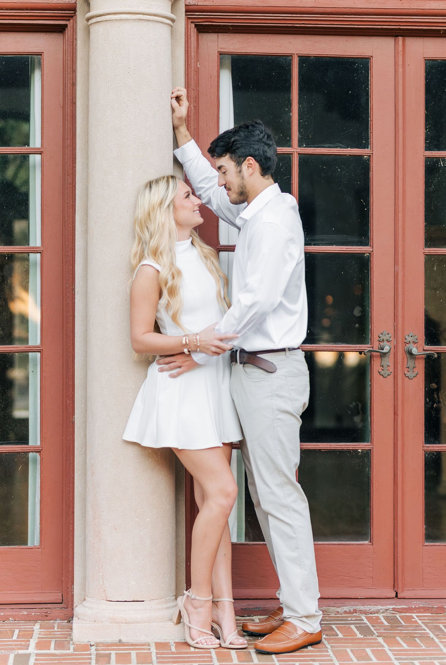A couple in white outfits dances together on a brick patio in a romantic sequence of dance moves.