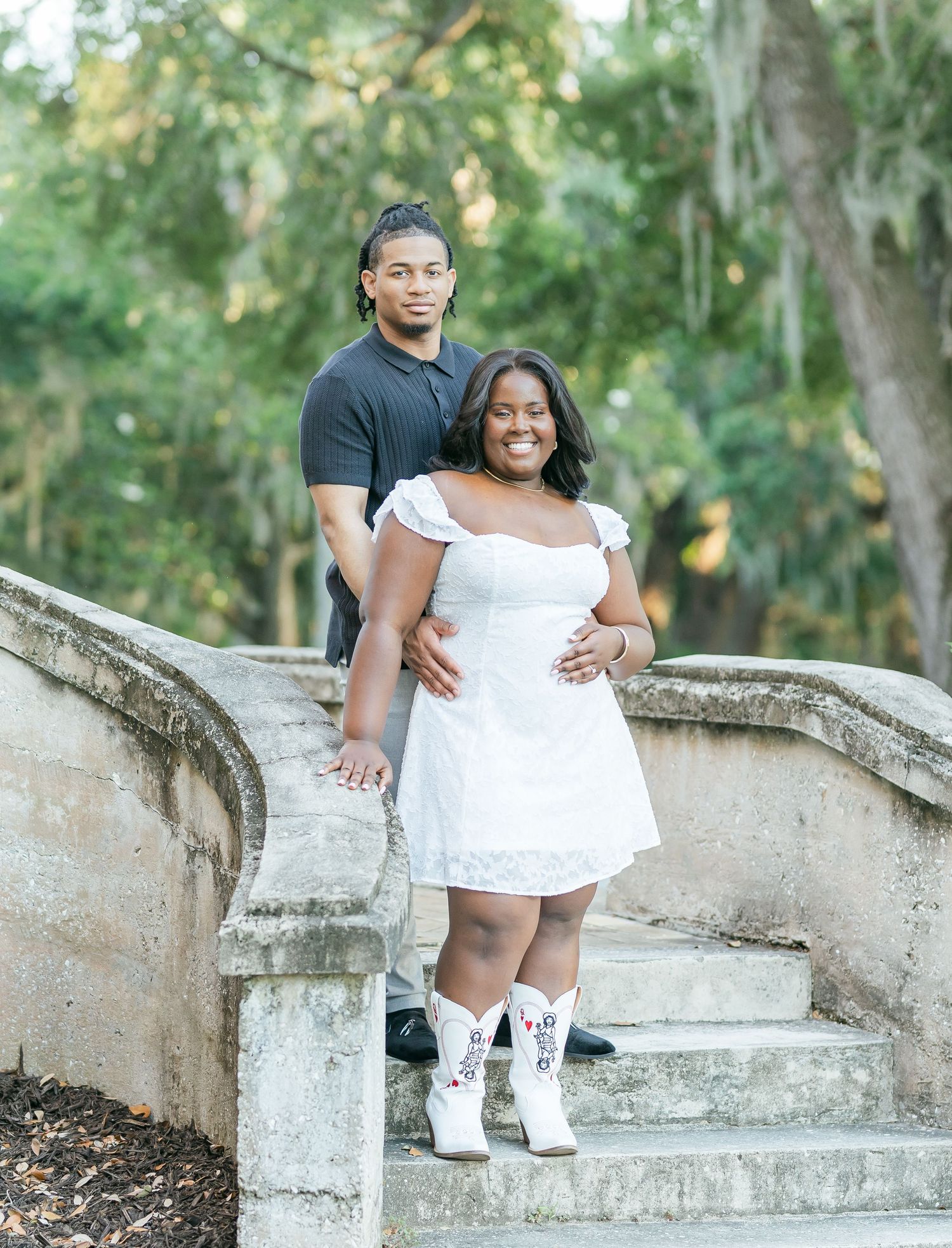 Romantic outdoor photoshoot featuring a couple posing on stone steps surrounded by greenery.