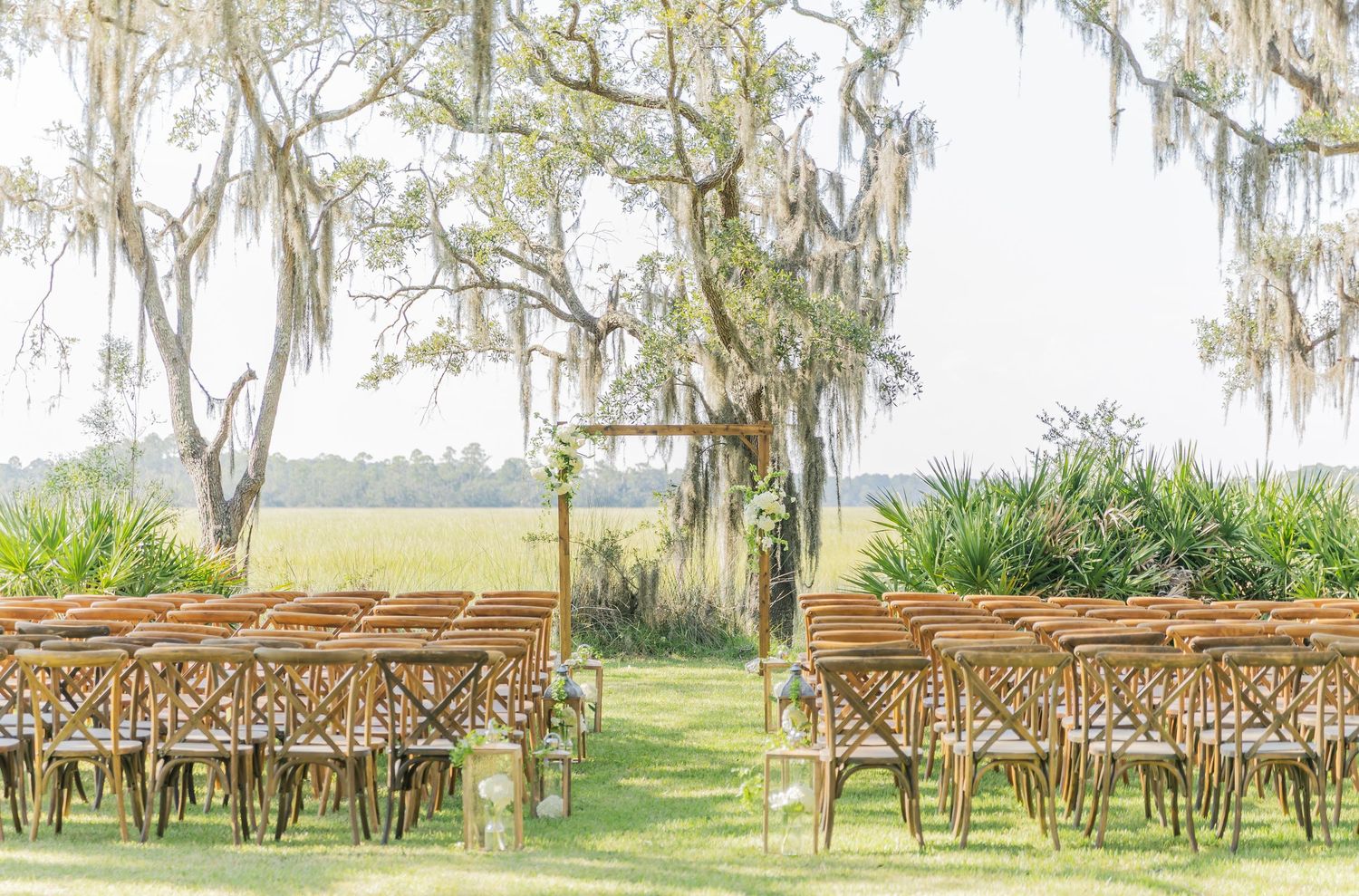 Wooden cross-back chairs set up in rows for an outdoor ceremony with Spanish moss hanging from trees.