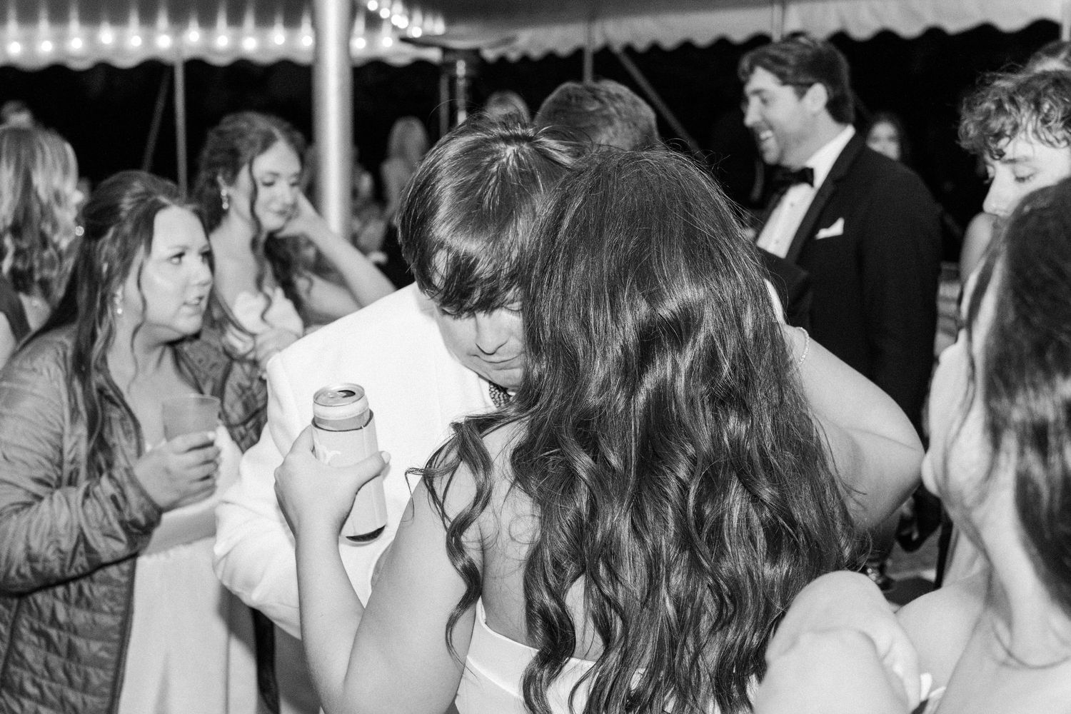 Black and white photo of wedding guests socializing and dancing at a lively outdoor reception under a tent.