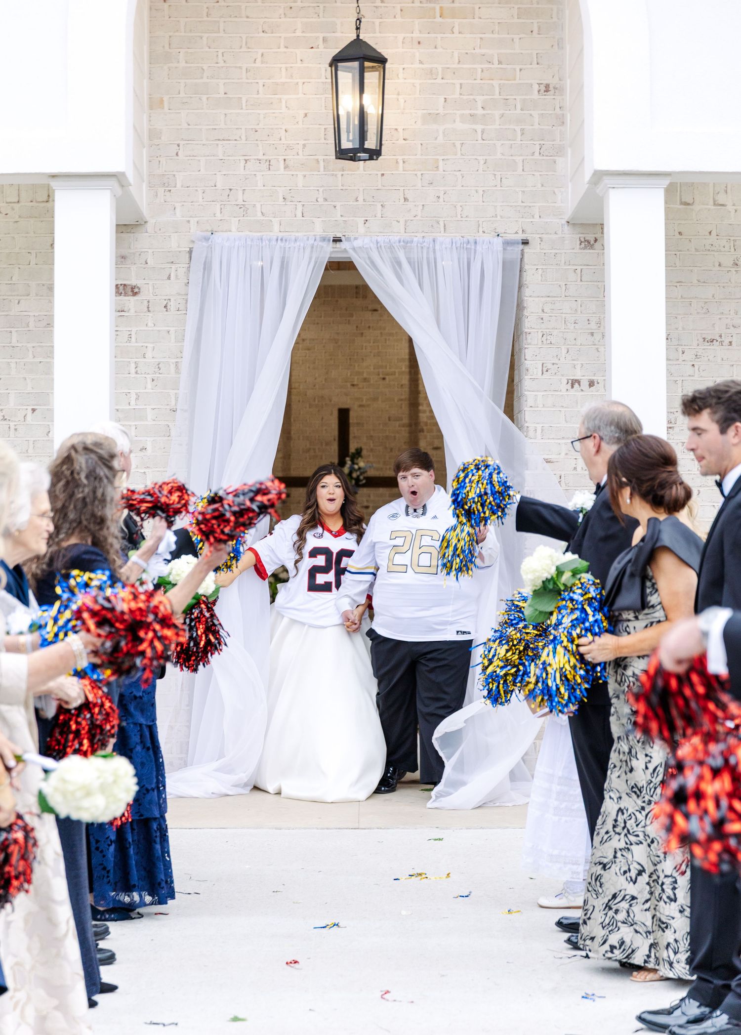 Bride and groom in football jerseys exit ceremony through cheerleader pom-pom send-off tunnel.