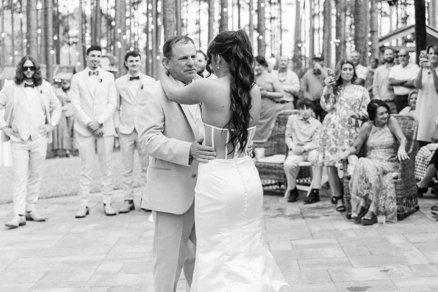Bride and father share emotional first dance in black and white photo at outdoor wedding reception.