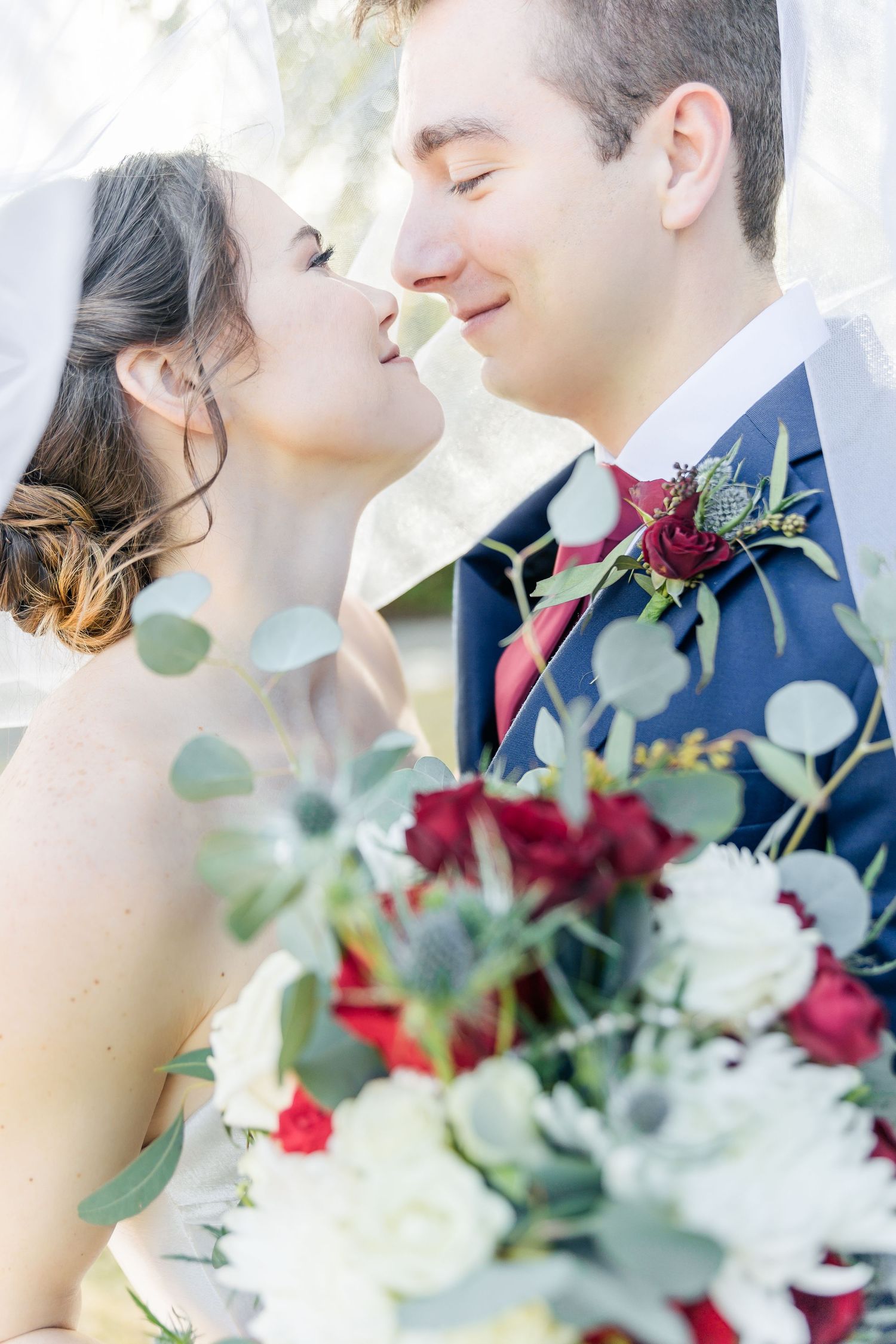 Romantic close up wedding photography with bouquet of red roses and eucalyptus leaves in foreground.