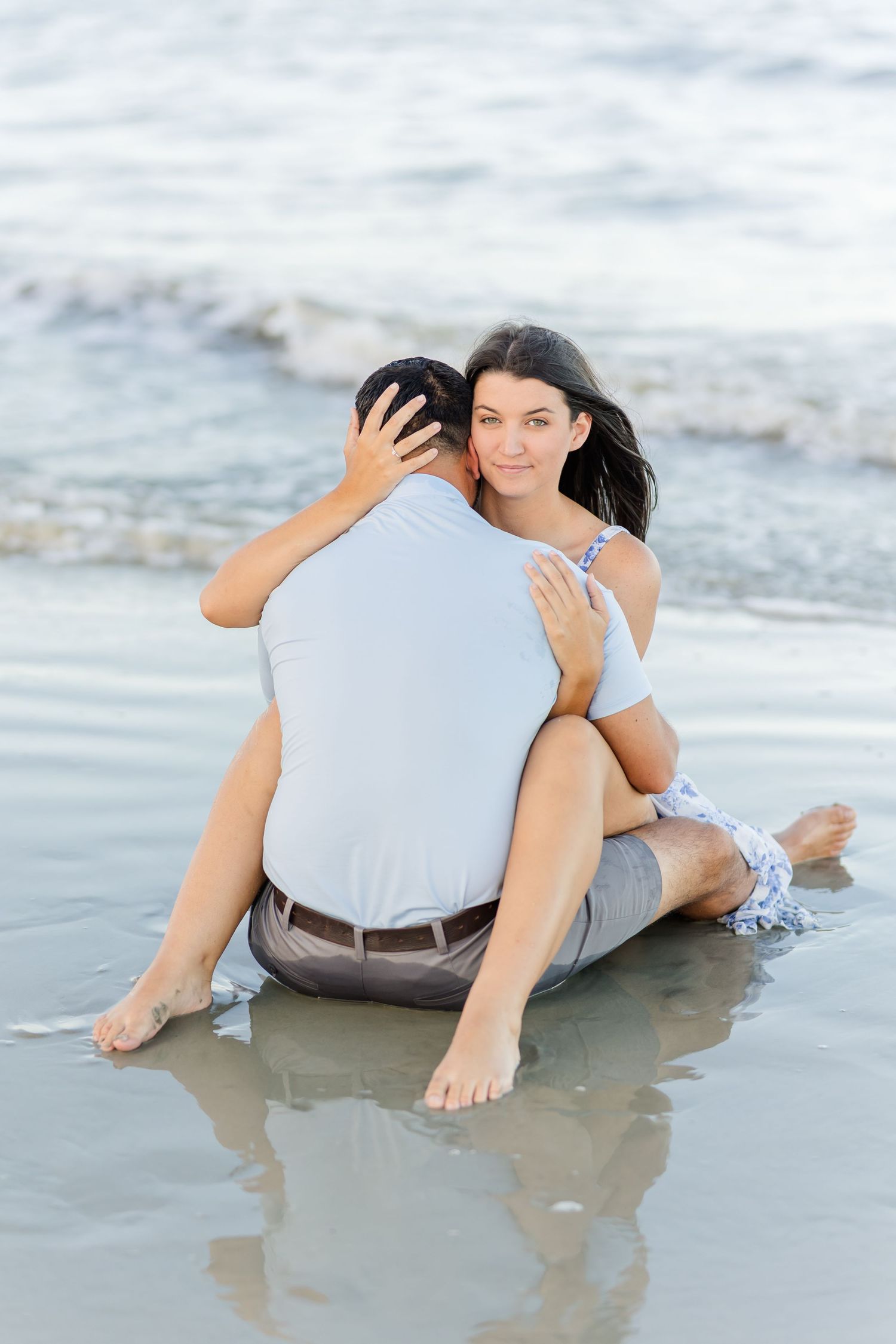 Romantic couple lies on wet sand at the beach shore as gentle waves wash around them at sunset.