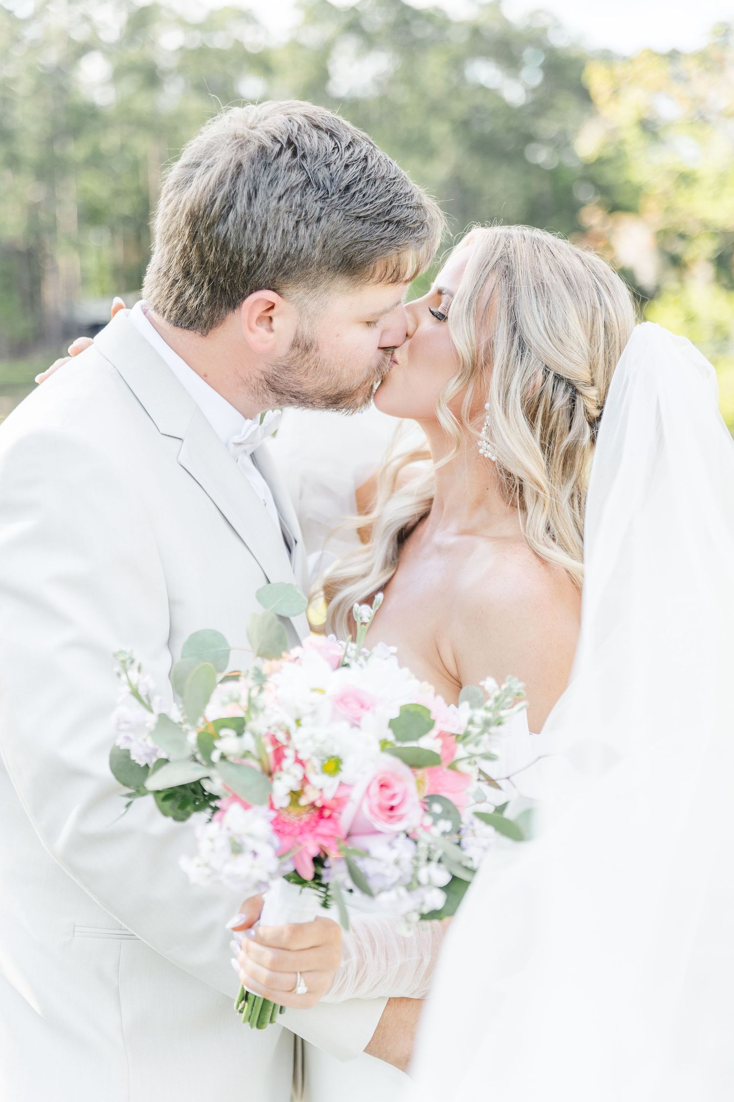 Ethereal wedding moment captured as couple shares a kiss against a dreamy outdoor backdrop.
