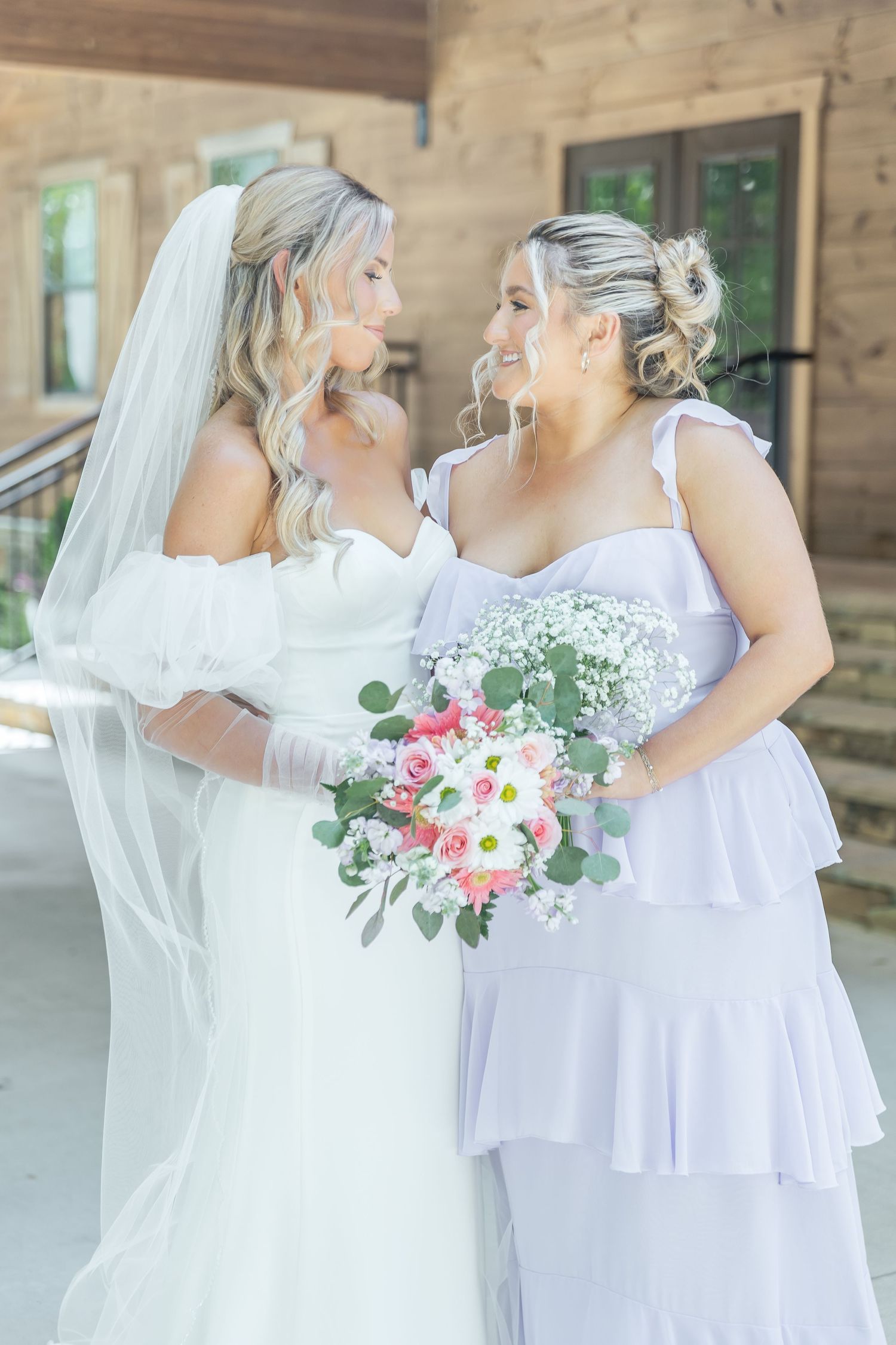 A close-up portrait of wedding attendants in white and lavender gowns holding pink floral bouquets.