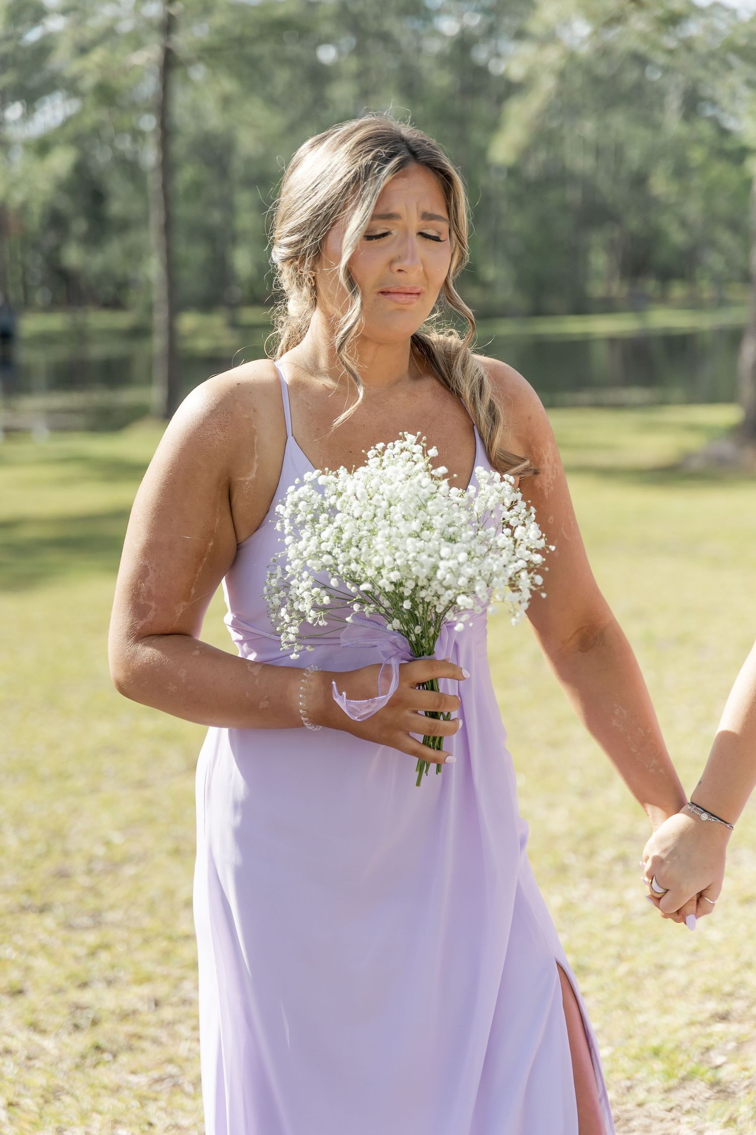Bridesmaid in lavender dress holds delicate baby's breath bouquet at outdoor wedding.