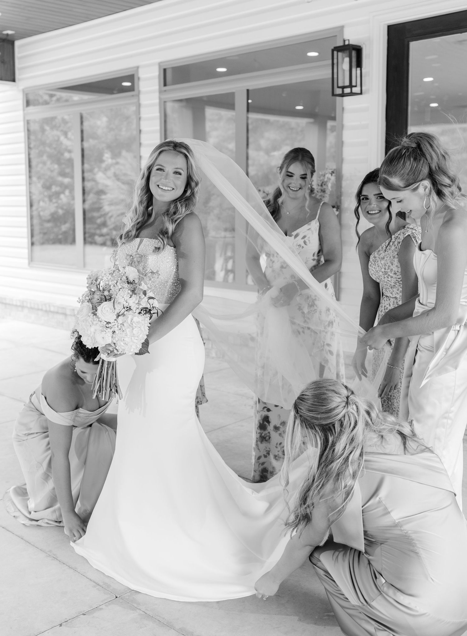 Black and white photo of bridesmaids adjusting bride's veil and train in strapless wedding gown.