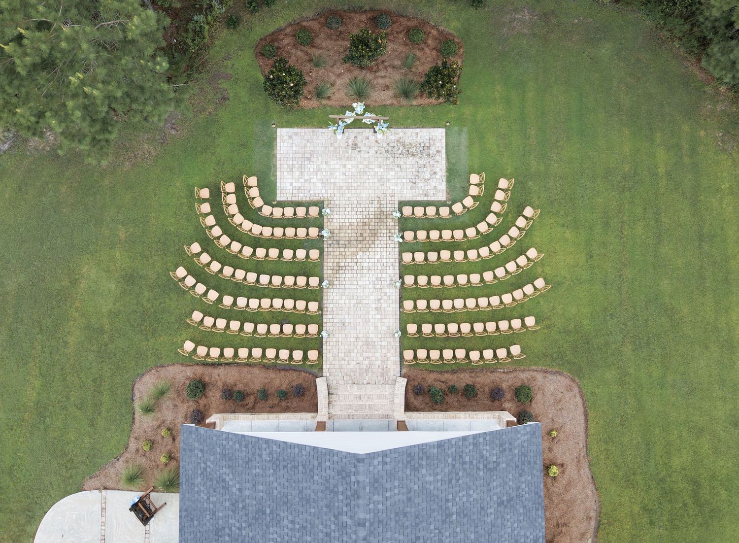 Aerial view of chairs arranged in a cross shape on green grass near a church building.