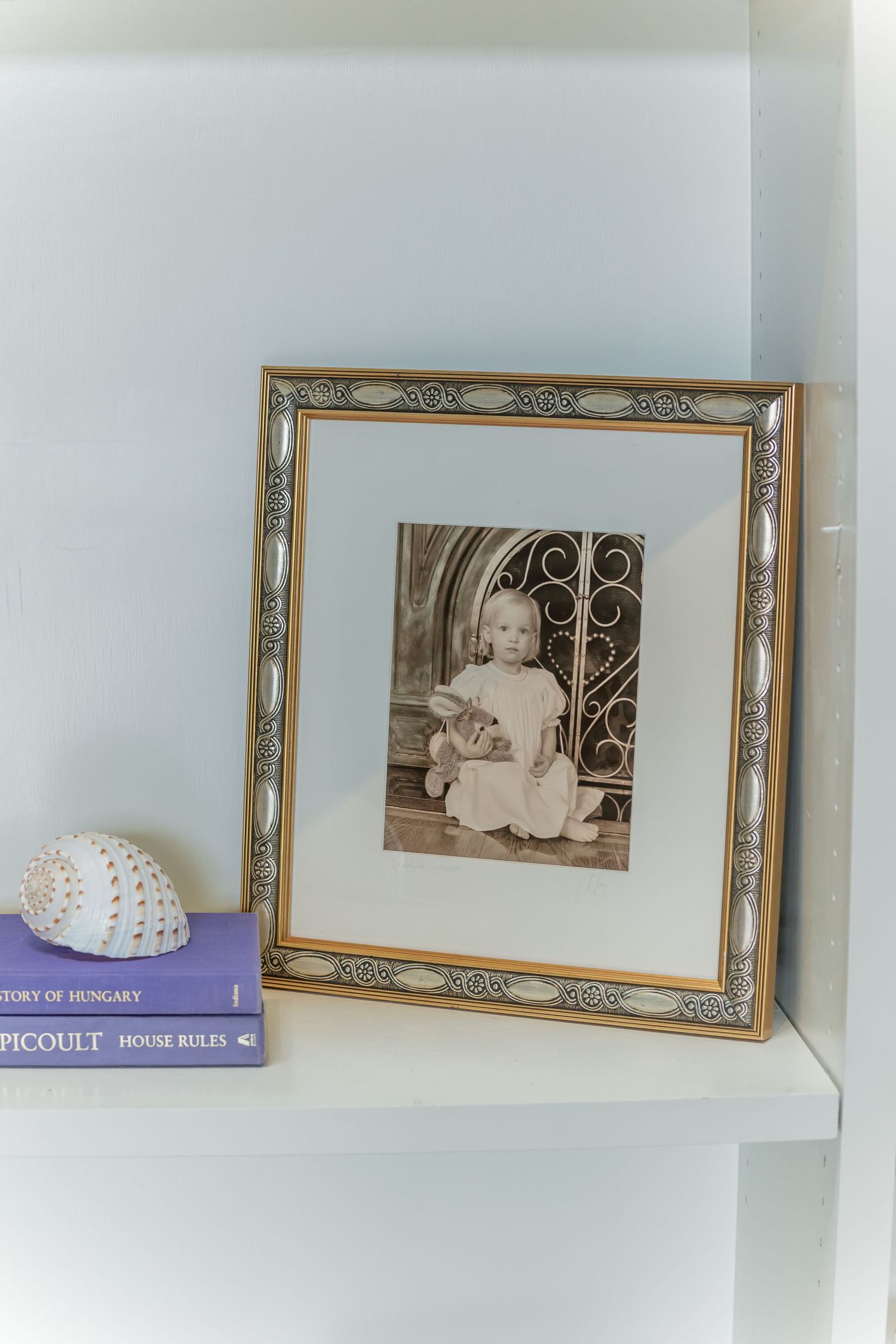 Vintage photograph in an ornate gold frame displayed on a shelf with books.