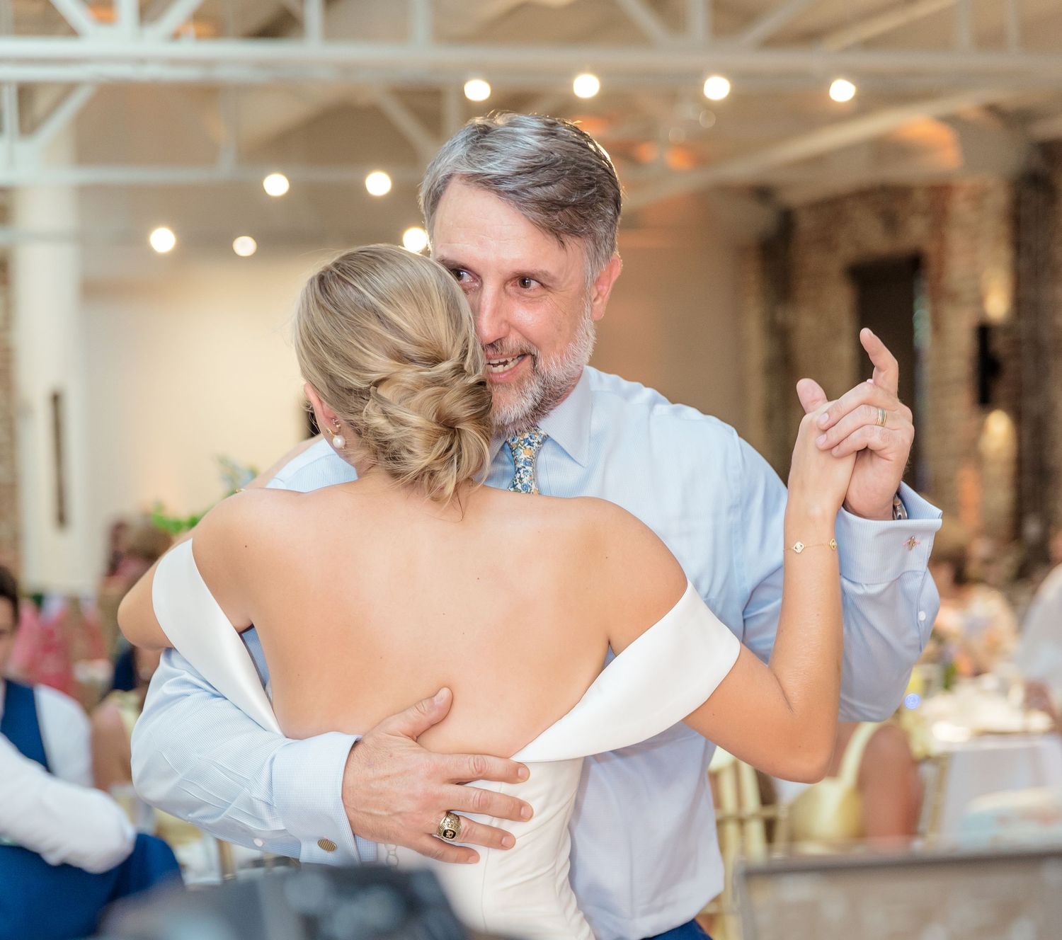 A couple dances together in a bright reception hall with romantic lighting and white decor.