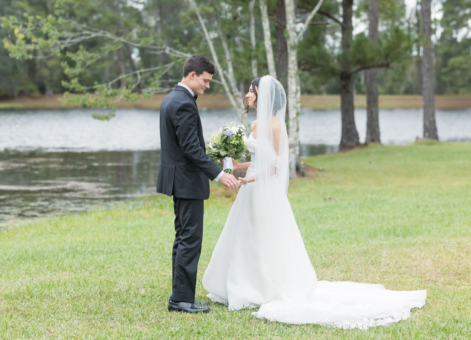 A bride and groom share a sweet moment by a lake during their outdoor wedding photoshoot.