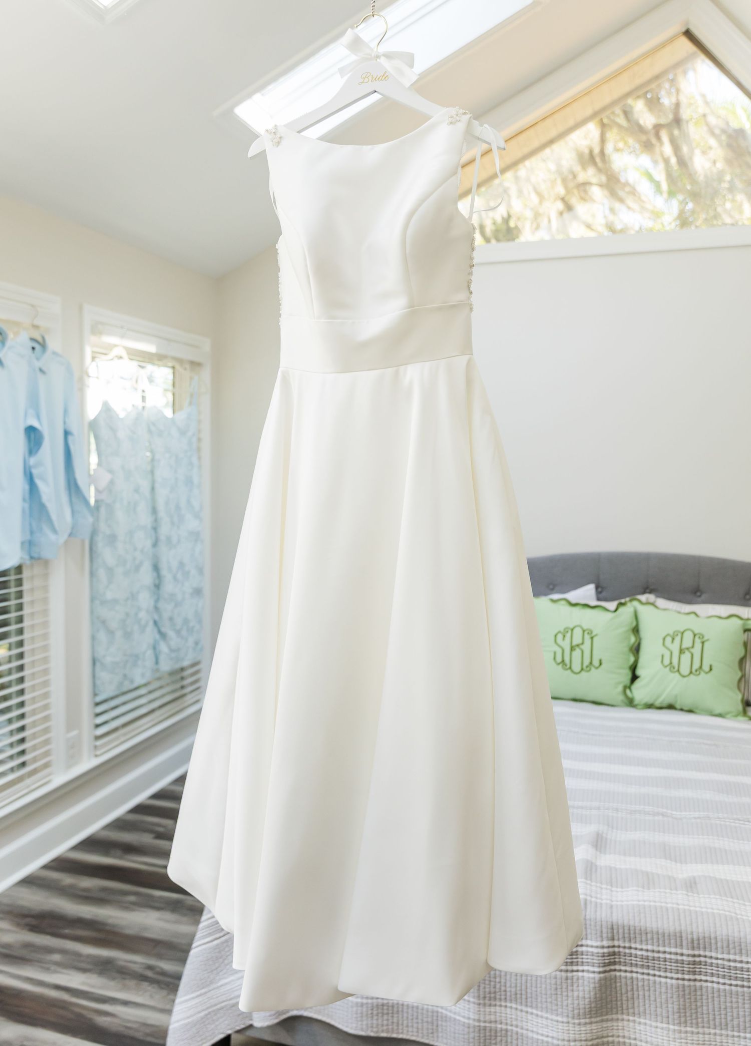 White cotton baptism gown with monogrammed initials displayed on a dress form against a bright window background.