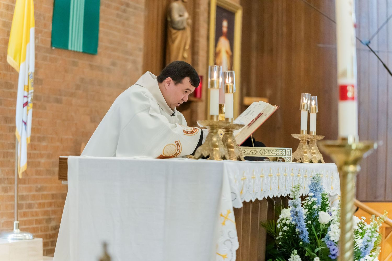 Interior of a brick Catholic church decorated with floral arrangements and religious symbols.