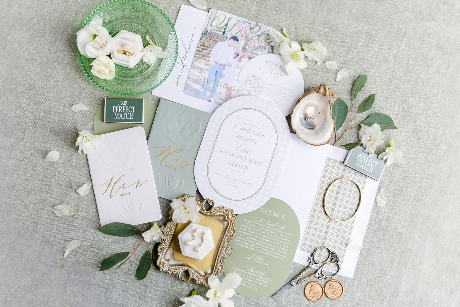 Wedding invitation suite with white flowers and green accents on a light gray background.