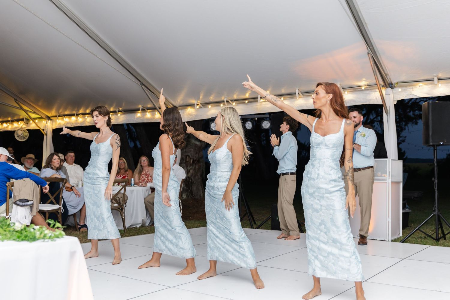 People dancing in a line formation under a white tent at a wedding reception celebration.