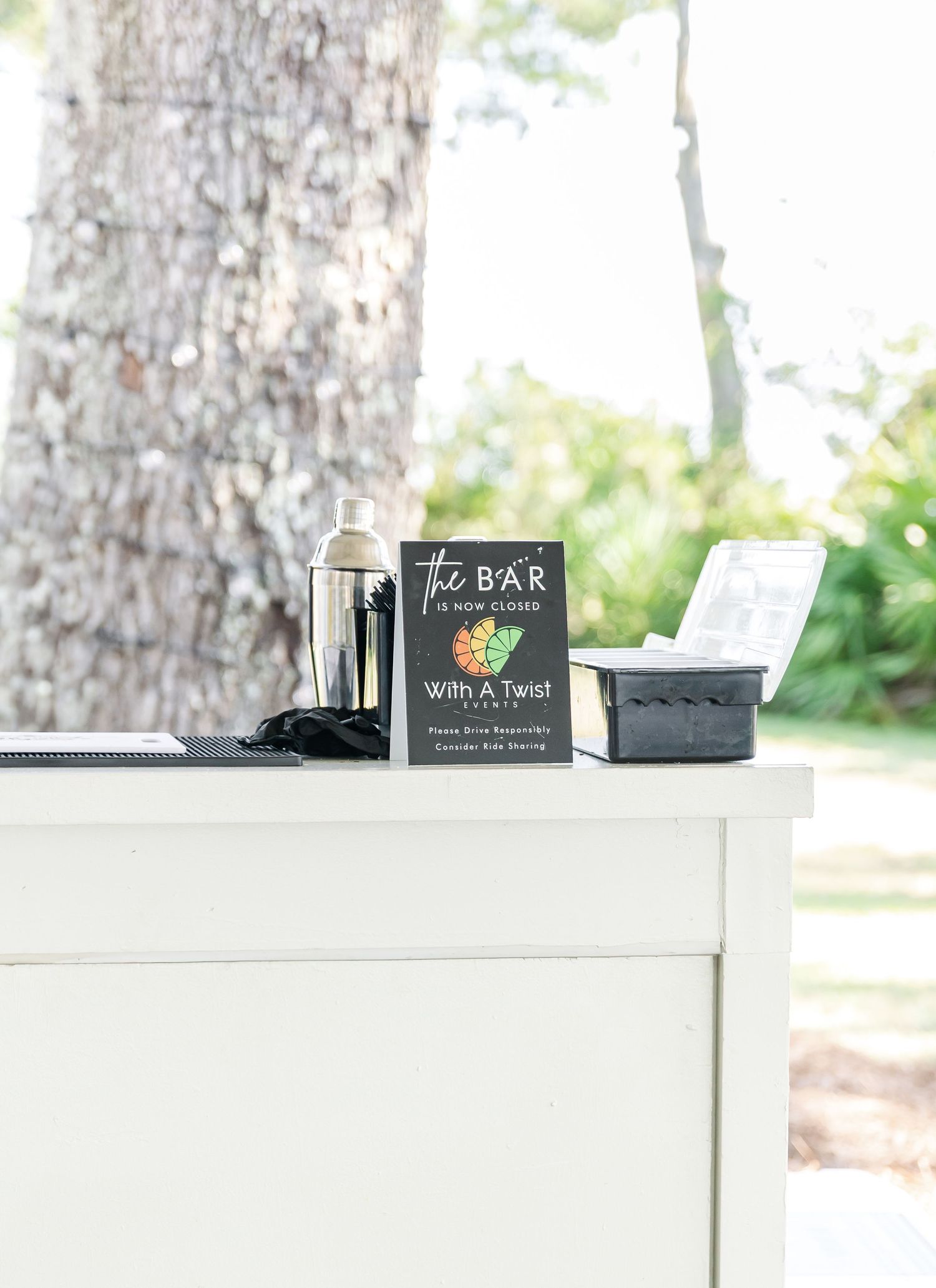 White bar setup with black signage and decorative elements against a rustic outdoor backdrop.