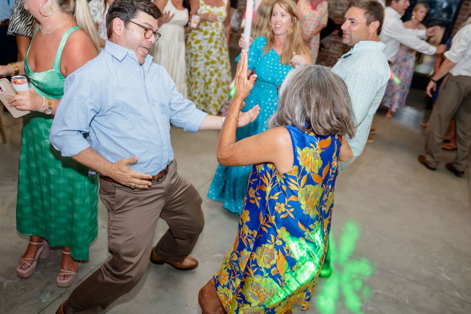 Wedding guests in colorful summer dresses dancing with glow sticks at reception.