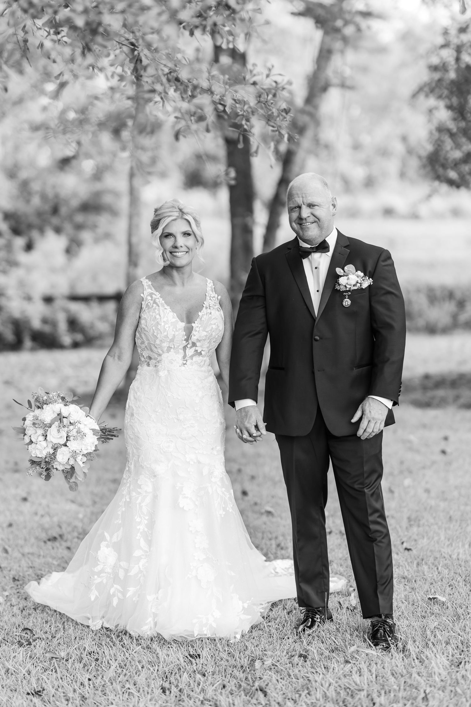 A romantic wedding couple poses together on a grassy lawn in black and white photography.