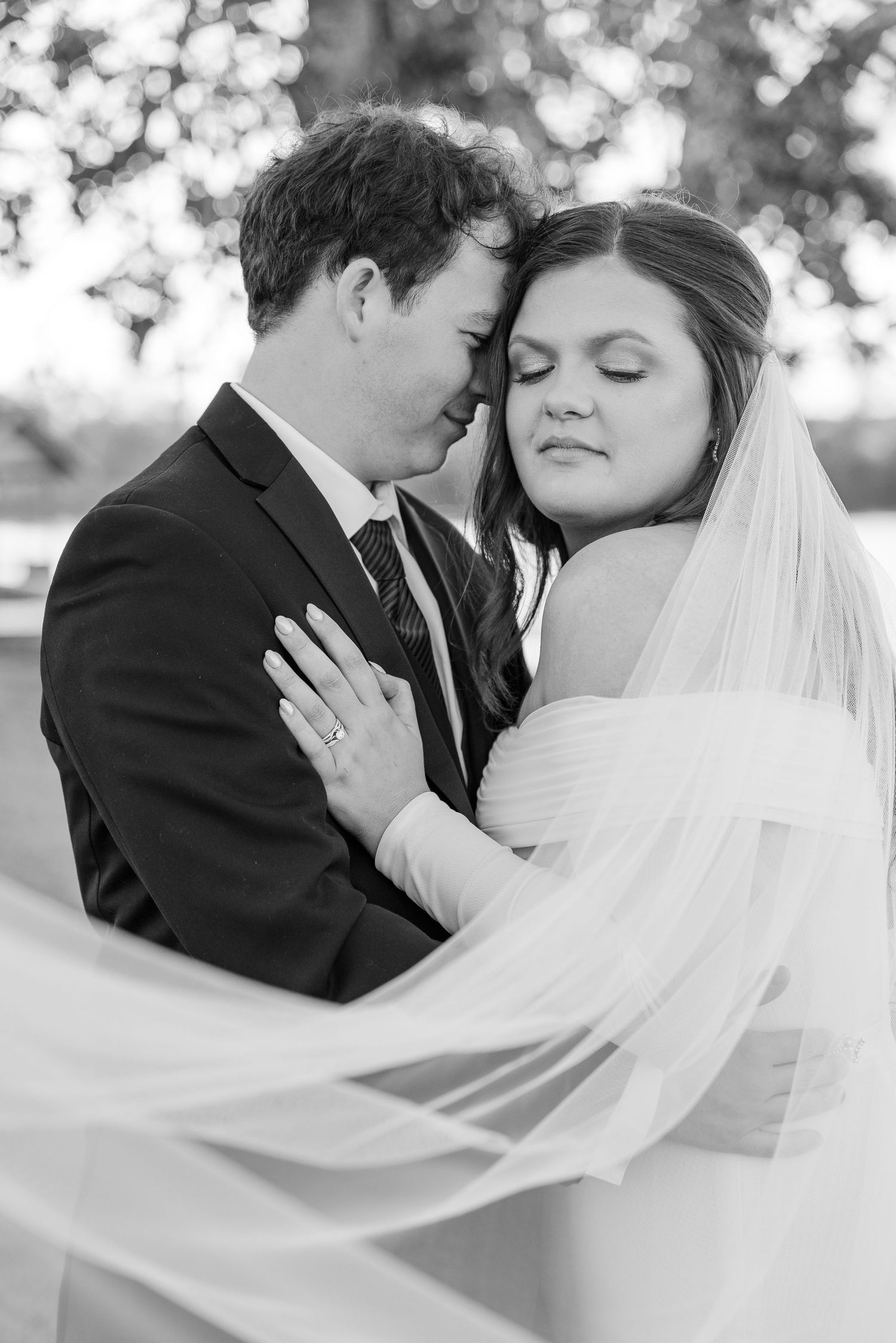 Intimate black and white wedding portrait with flowing veil against natural backdrop.