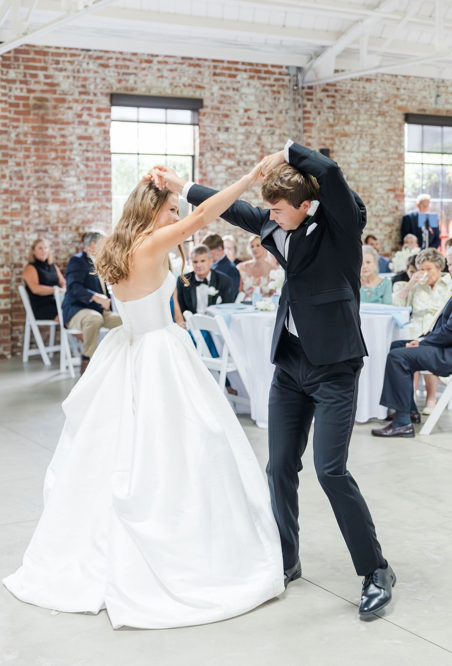 Bride and groom share joyful first dance spin at rustic brick wedding reception.
