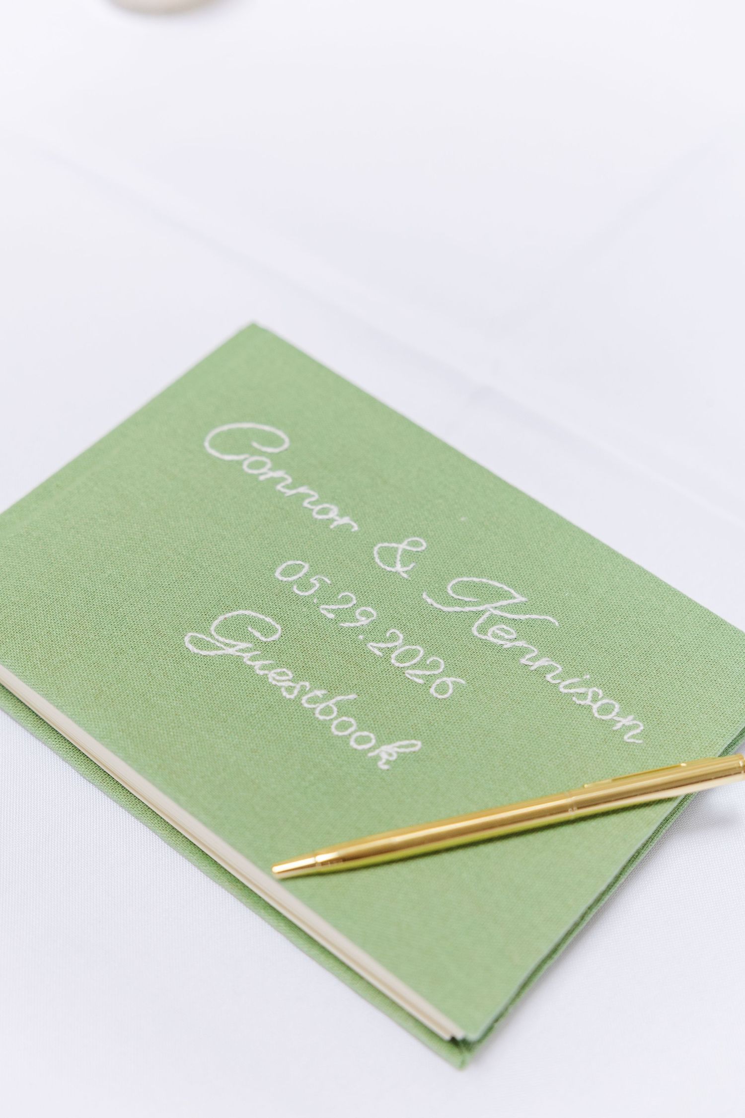 Green wedding guestbook for Connor and Kennison dated 05.29.2026 with a gold pen.