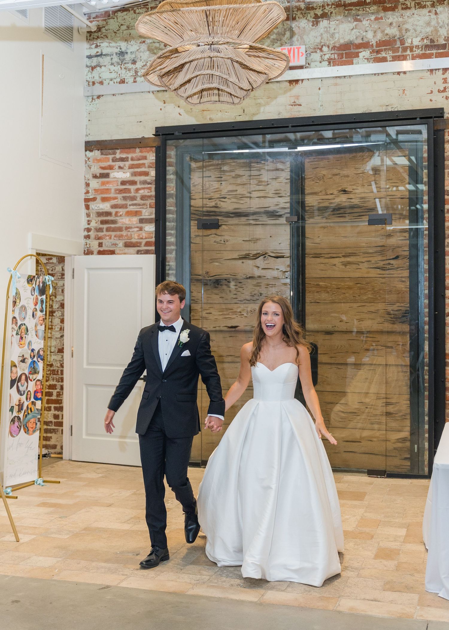 Excited newlyweds enter reception hand in hand through industrial venue doors with brick backdrop.