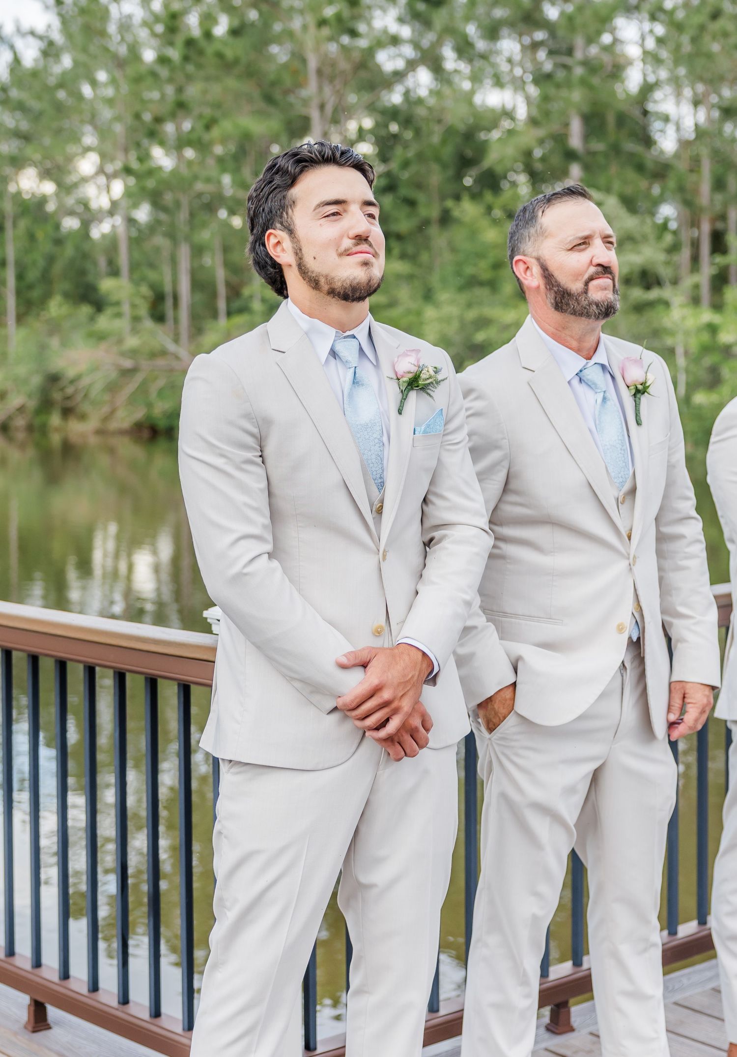 Groom and groomsman in beige suits with light blue ties stand at the altar overlooking a pond.