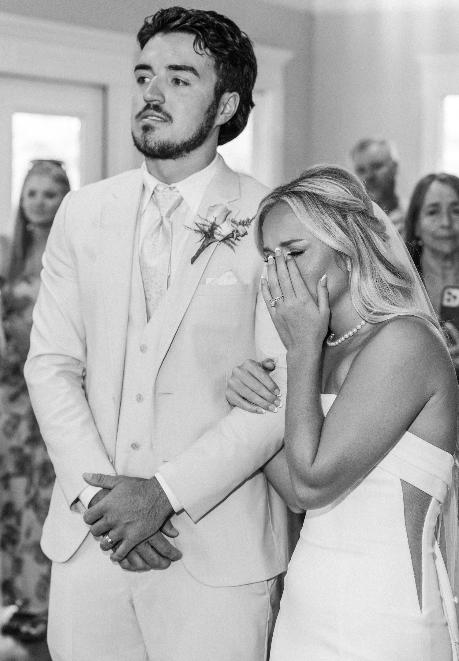 Emotional bride and groom share tearful moment during black and white wedding ceremony.