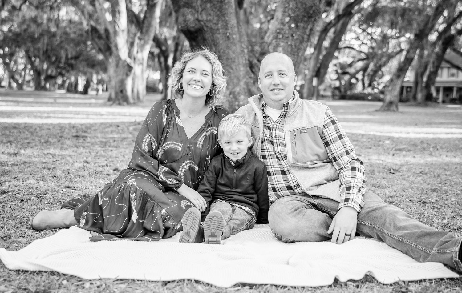 Black and white photo of family sitting together on blanket in park.