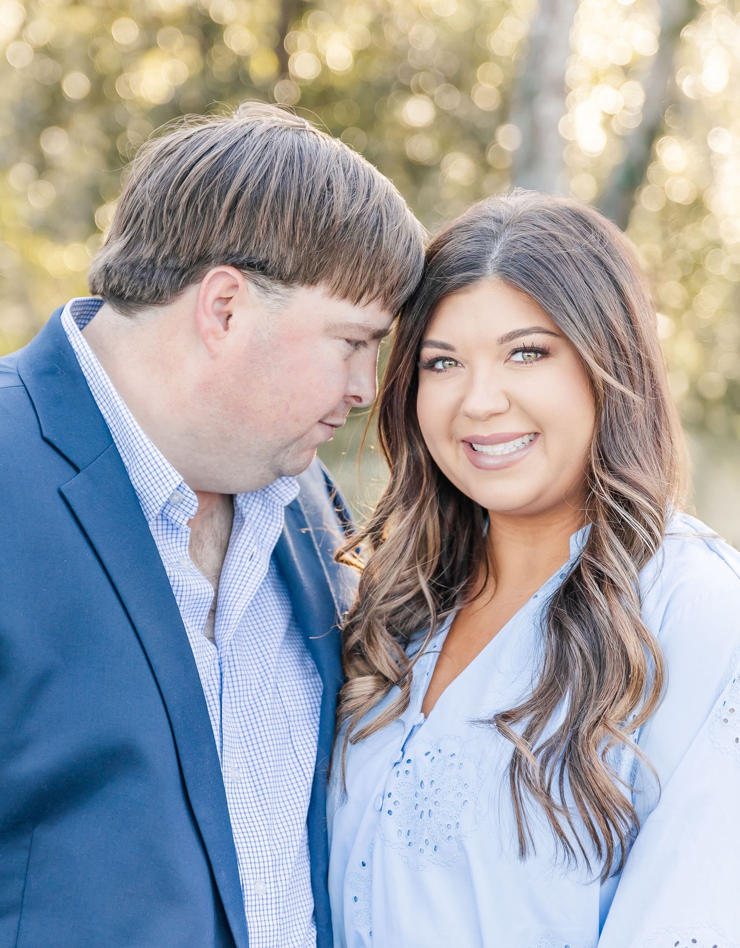 A close-up engagement photo showing a couple in coordinated outfits with soft bokeh lighting in the background.