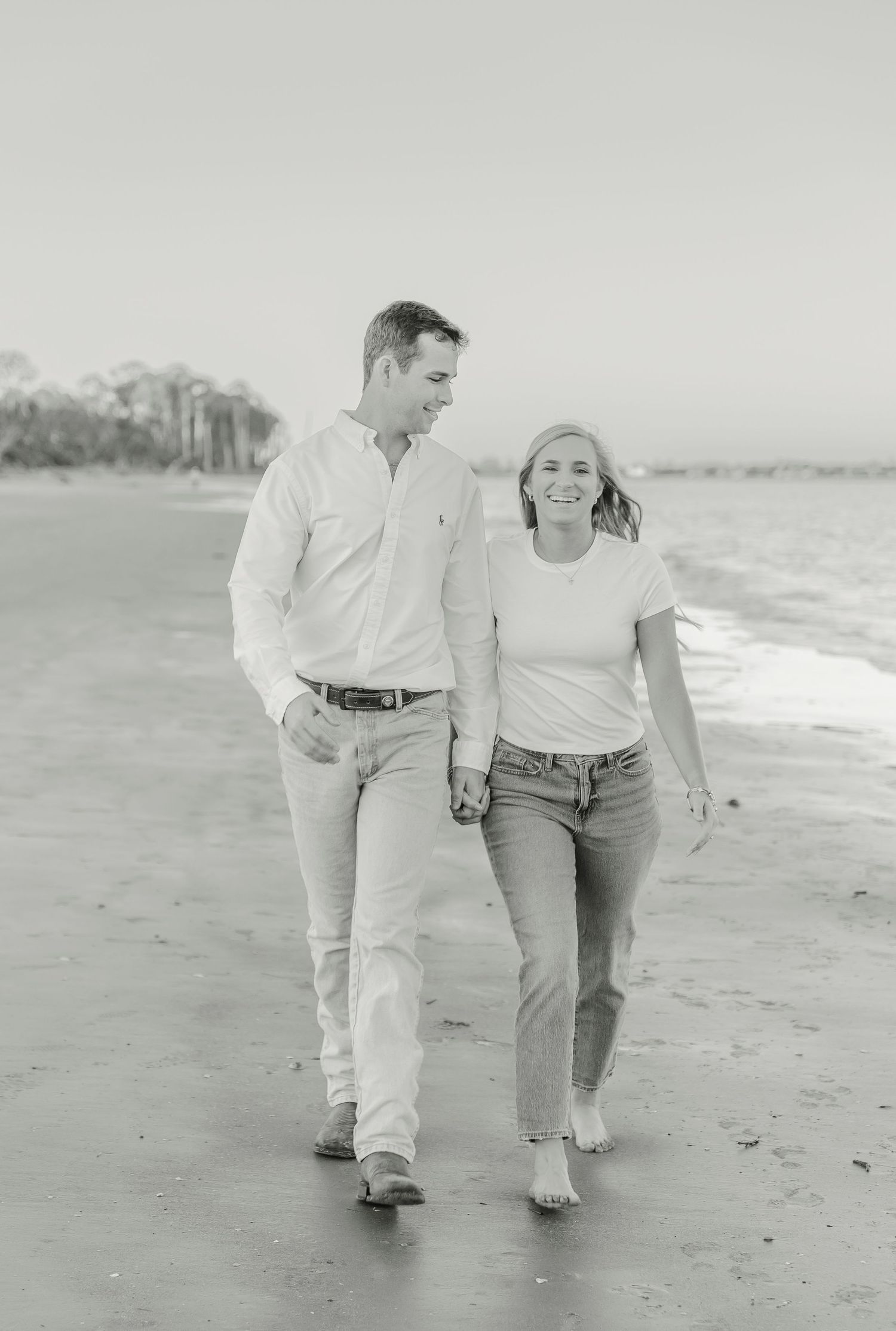 A couple takes a romantic beach walk in black and white photography.