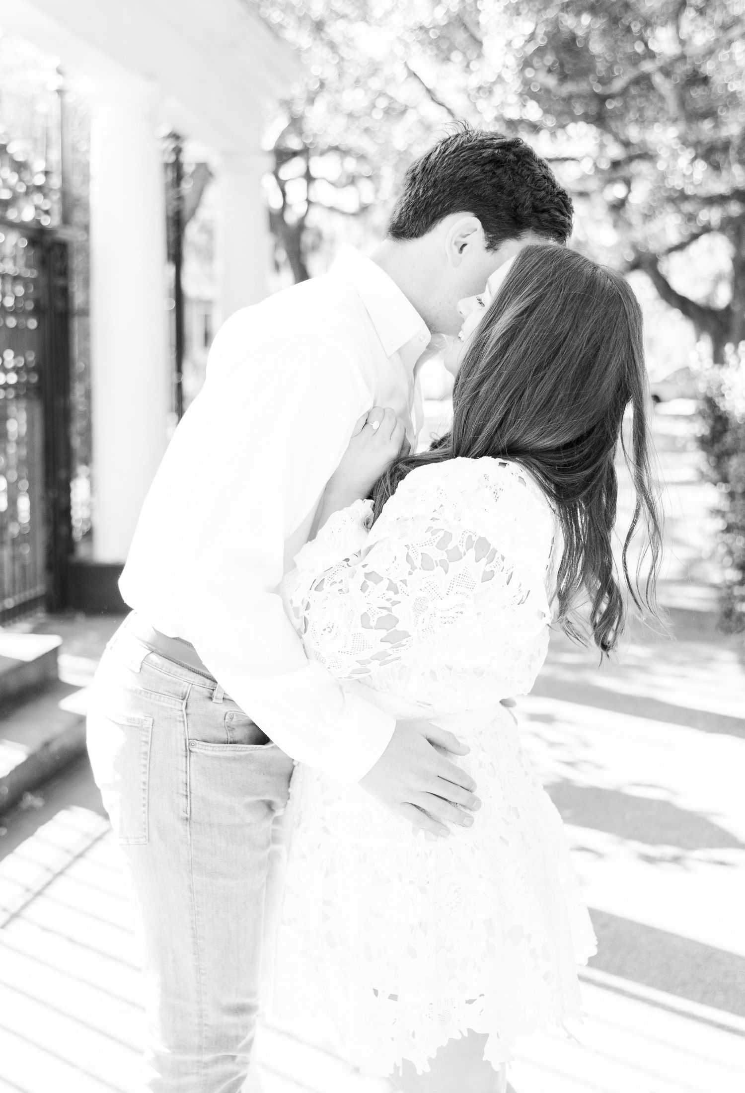 Black and white portrait of romantic embrace in sunlit garden setting.