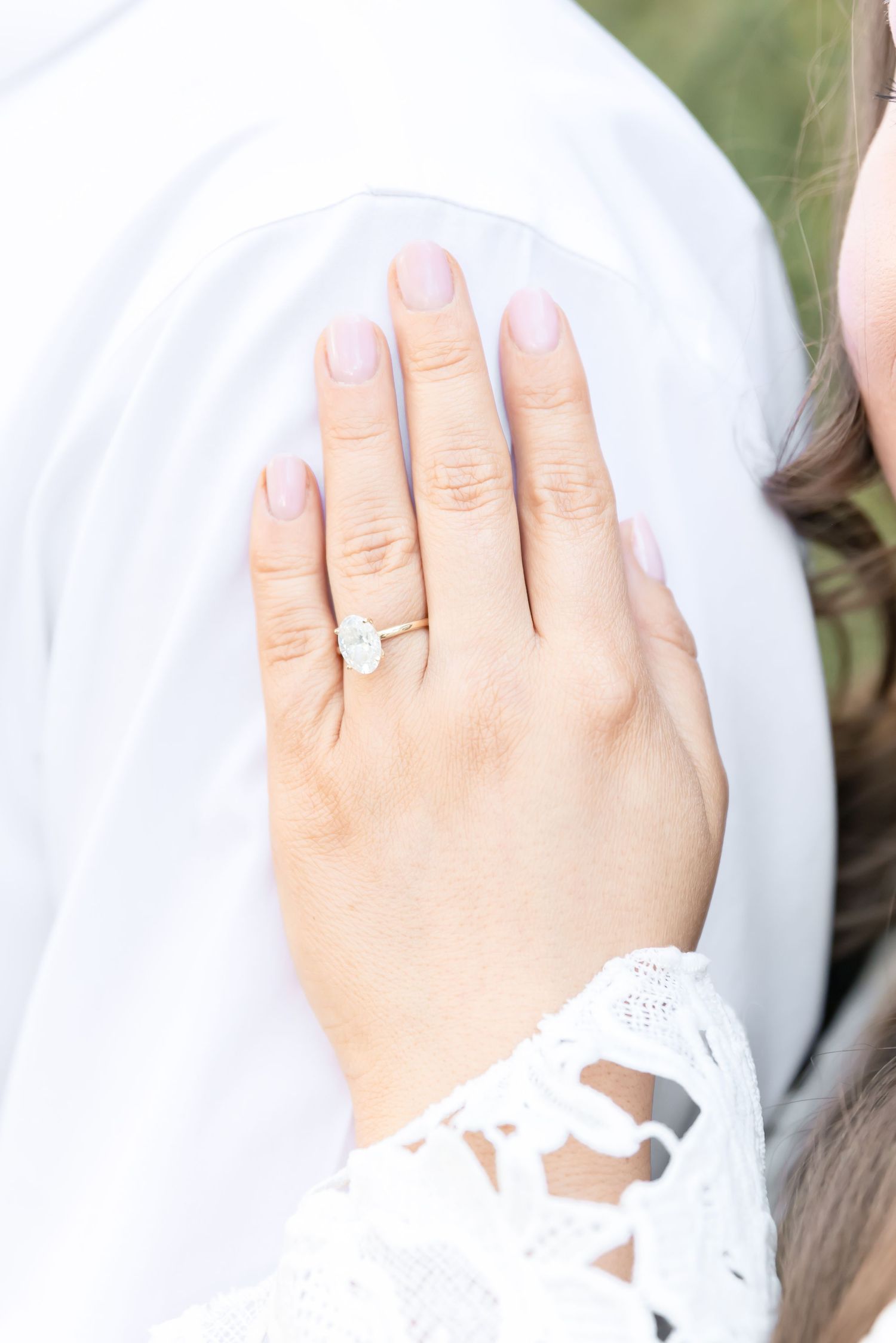 Close-up of an engagement ring on a woman's hand resting against white lace fabric.
