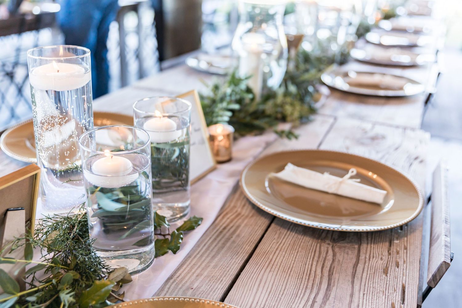 Wedding table decor featuring floating candles in glass vessels and gold charger plates.