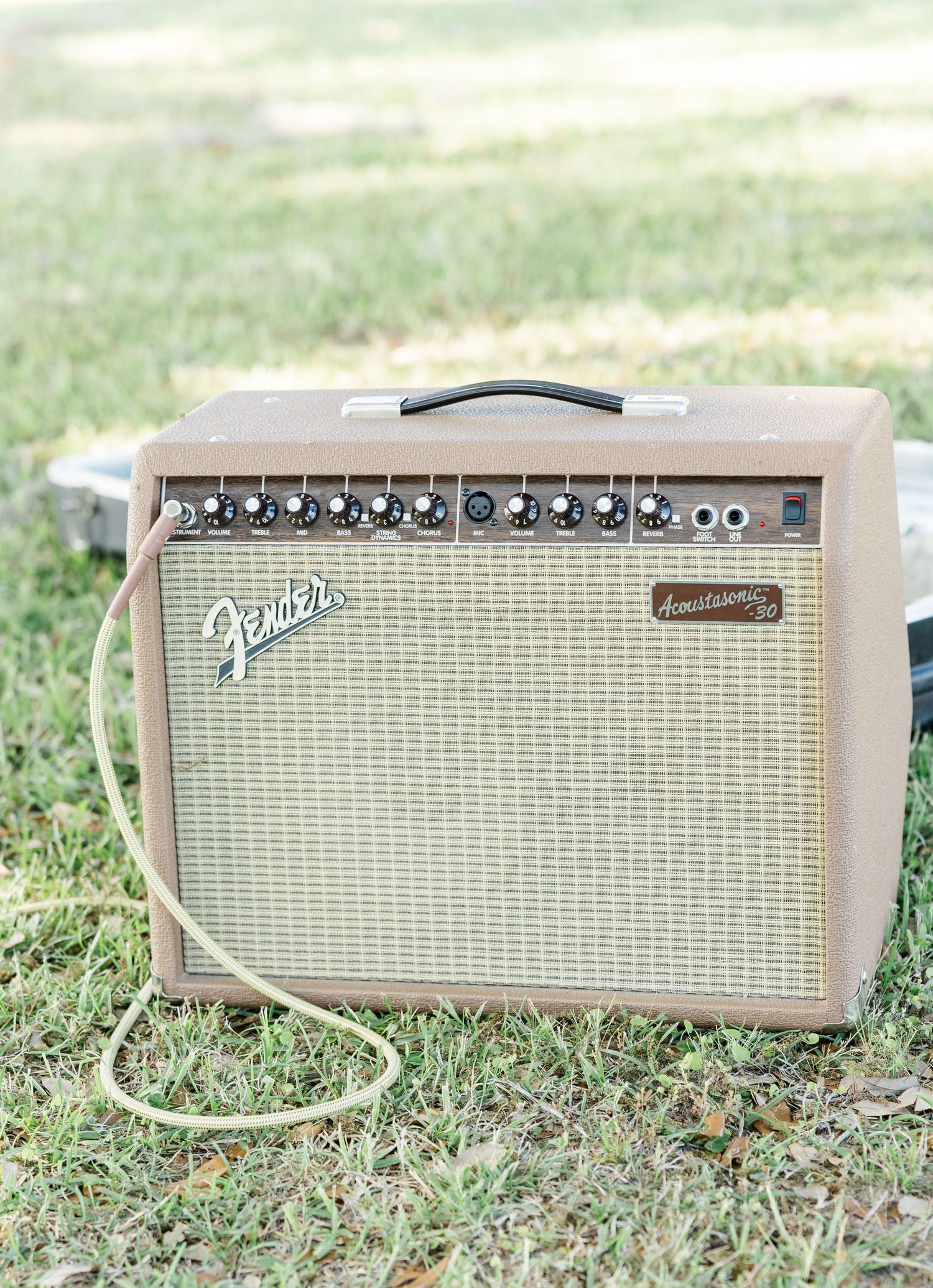 Vintage Fender Acoustasonic guitar amplifier sitting on green grass at an outdoor wedding venue.