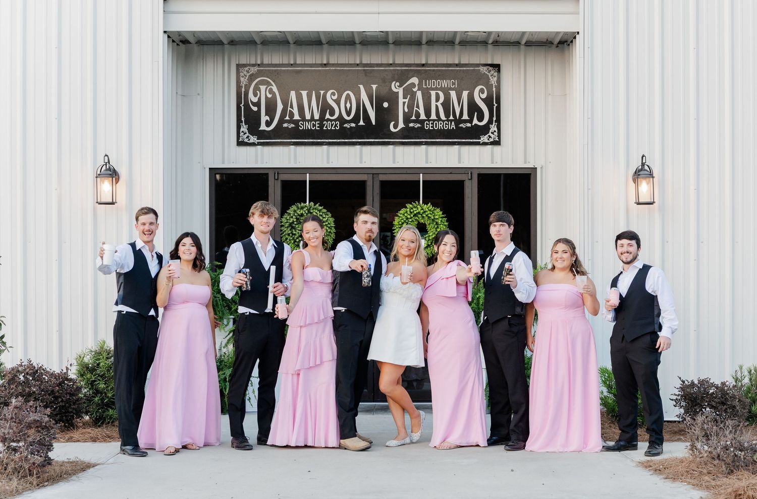 Wedding party in pink bridesmaid gowns and black suits posing outside Dawson Farms venue.