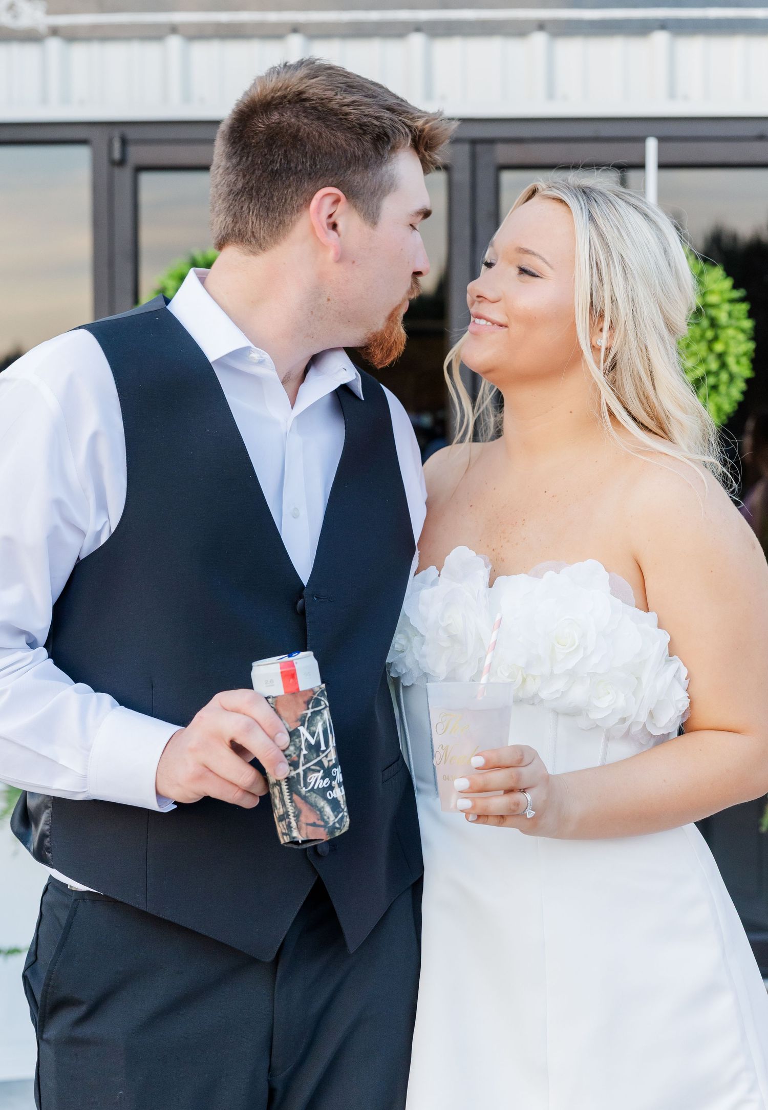 Bride in strapless white gown and groom in navy vest sharing a romantic moment outdoors.