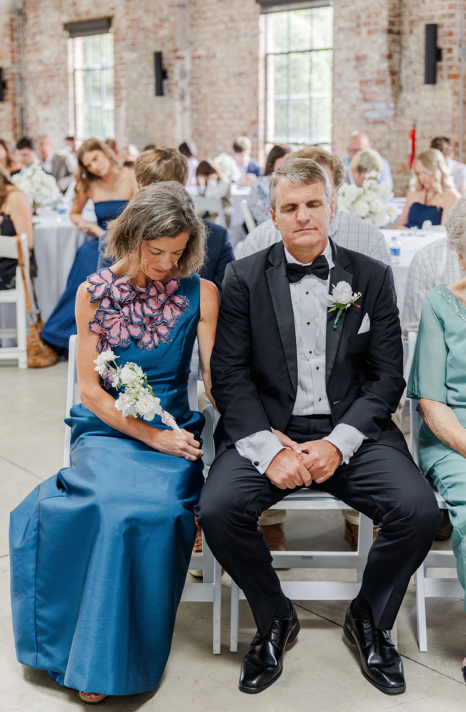 Parents of the couple seated at wedding ceremony in elegant blue and black formal attire.