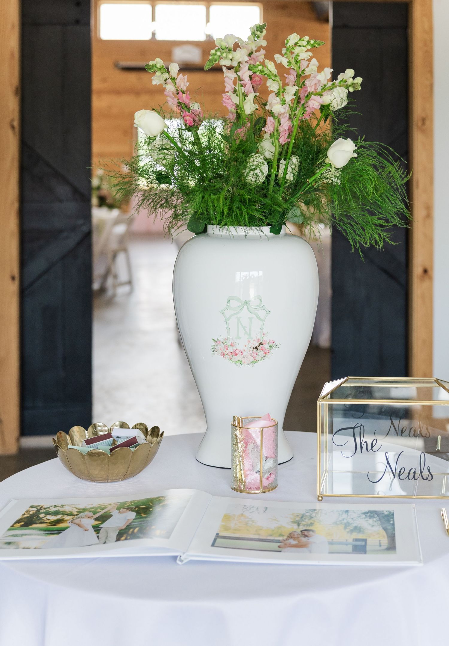 Elegant wedding guest book table with monogrammed white vase, pink floral arrangement, and personalized signage.