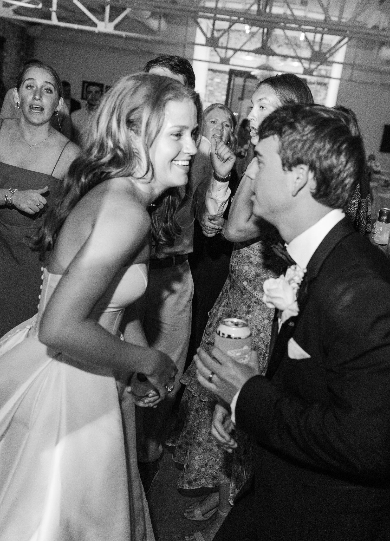 Black and white photo of laughing bride and groom dancing together at lively wedding reception.
