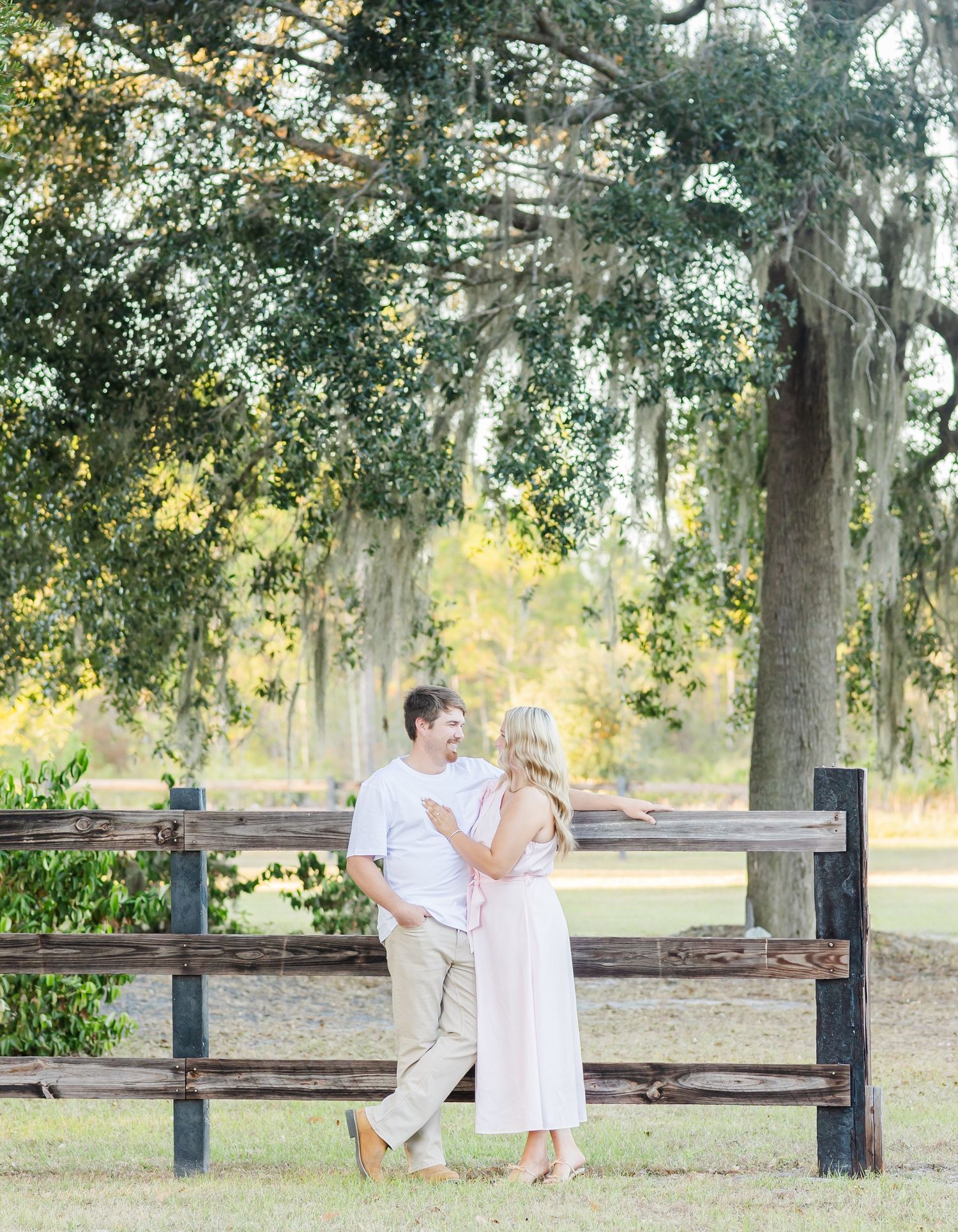 Couple sitting together on a wooden bench under moss-draped oak trees in a peaceful park setting.