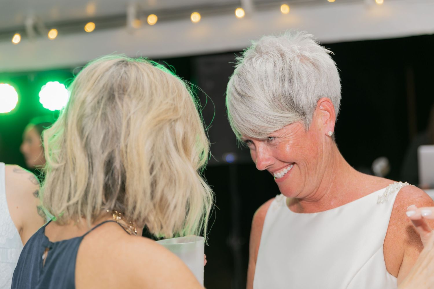 Guests dancing and socializing at a dimly lit evening reception with green lighting.