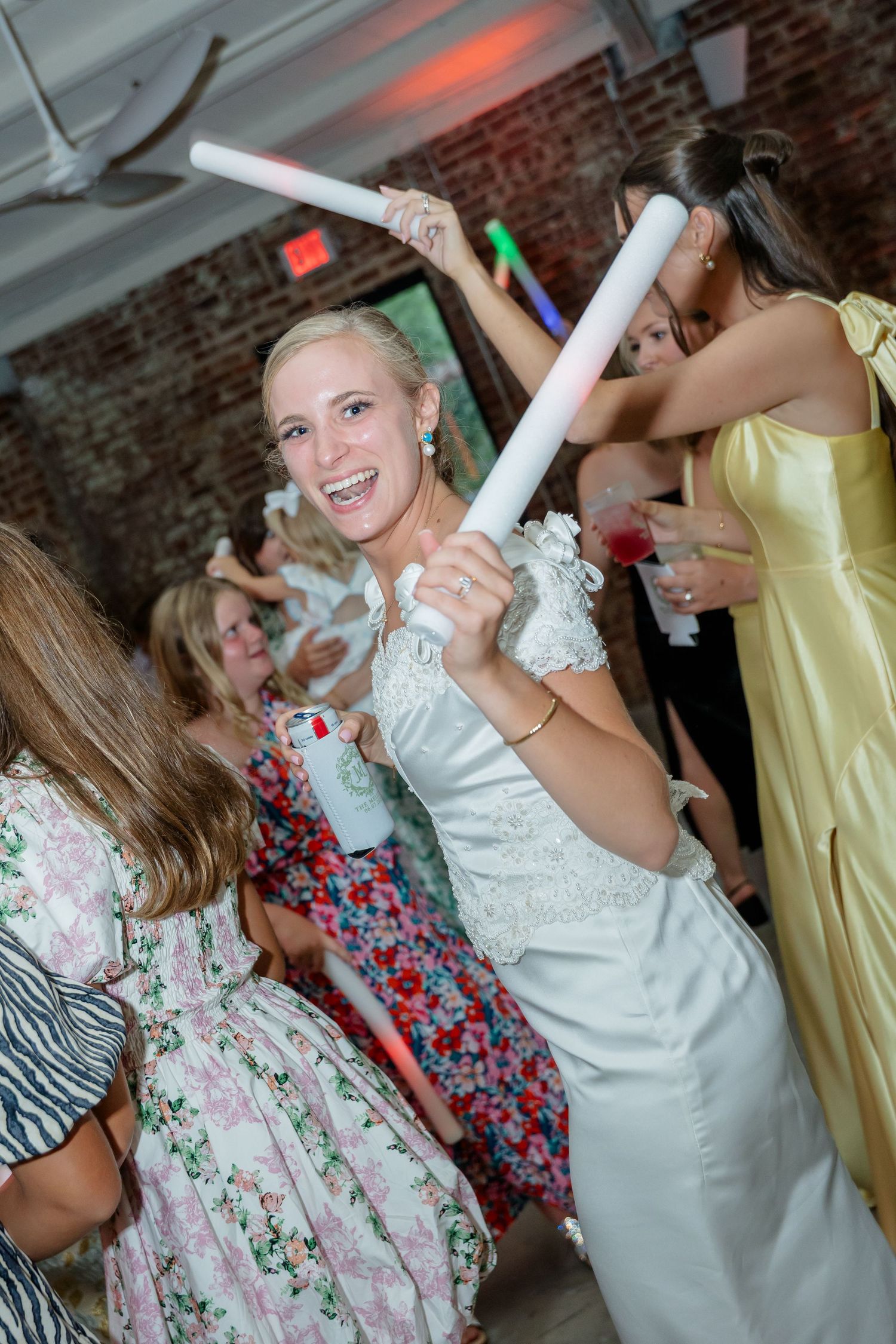 Wedding celebration with guests dancing in floral dresses under ambient lighting in a brick venue.